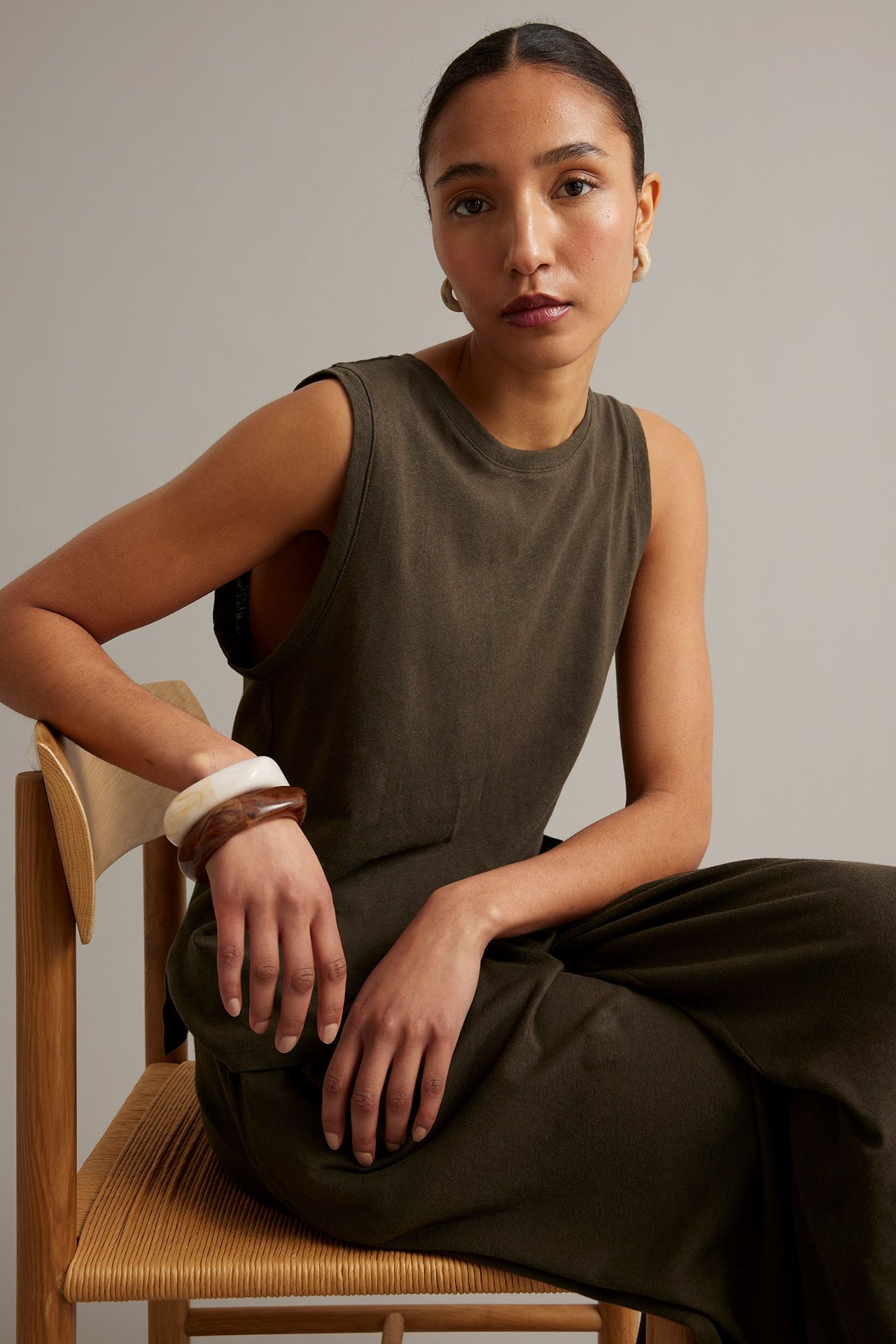 Kvinna bär ett brunt linne i bomull-linnemix, matchande vida byxor, ringörhängen och två armringar.