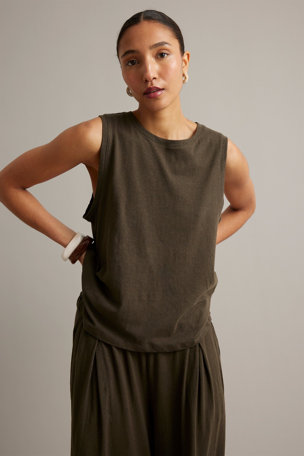 Framifrån: kvinna i mörkbrun linneblandad tanktopp, matchande culottebyxor, vita örhängen och armband.