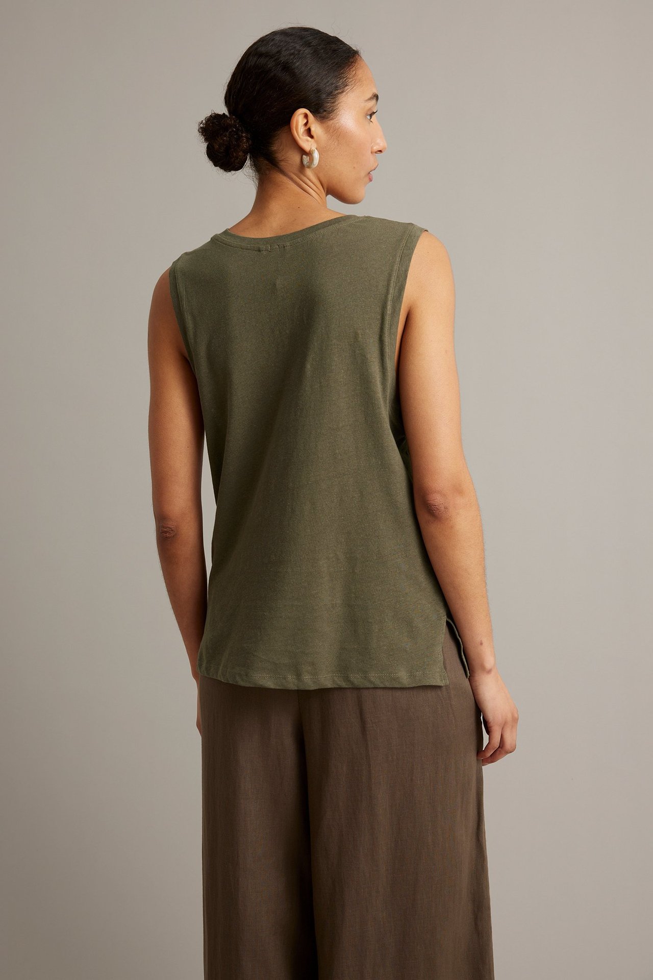 Ryggvy av en kvinna i en lös kakigrön linneblandad tanktopp med bruna vida byxor.