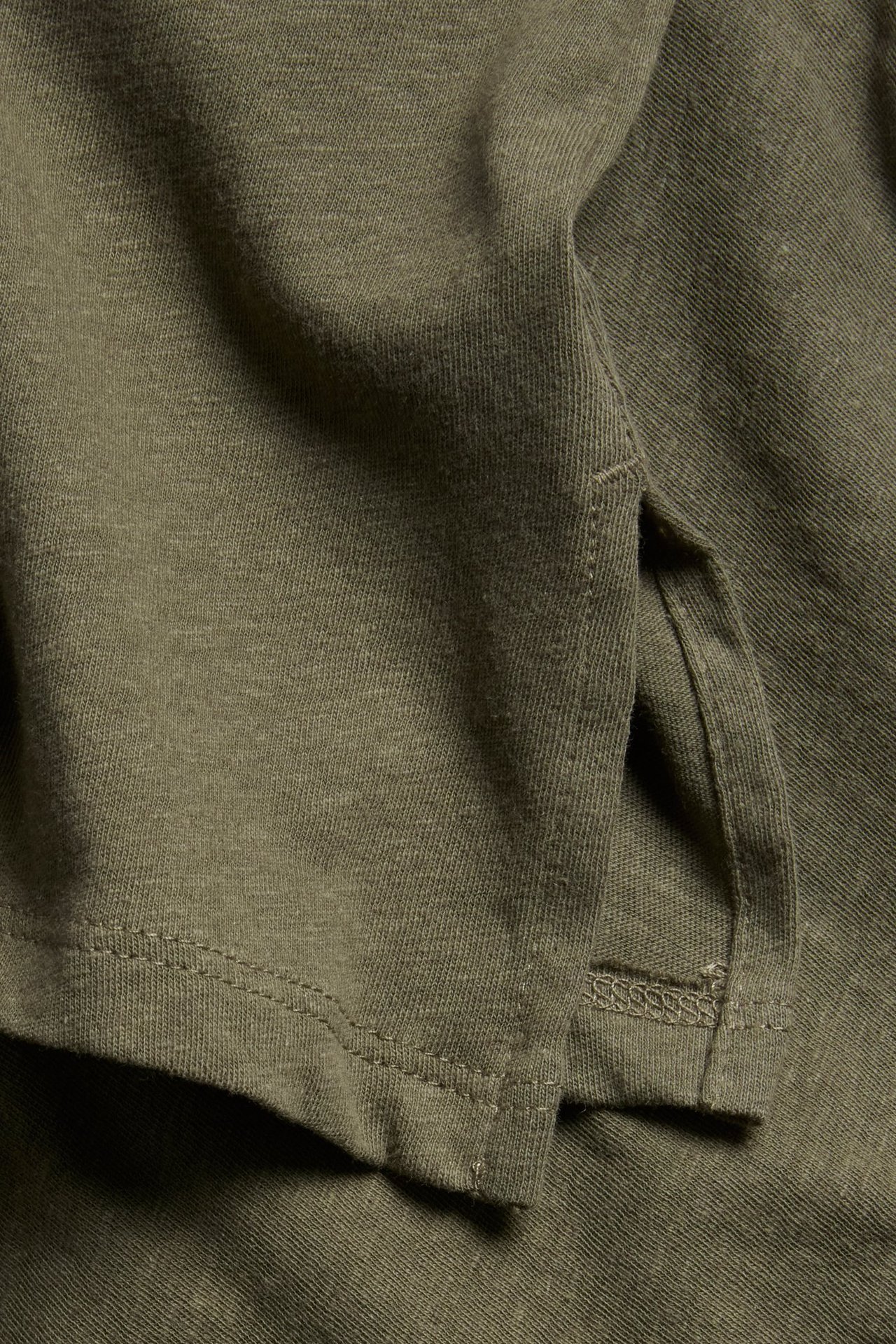 Närbild av en khakigrön enfärgad topp i linne- och bomullsmix med sidoslits.