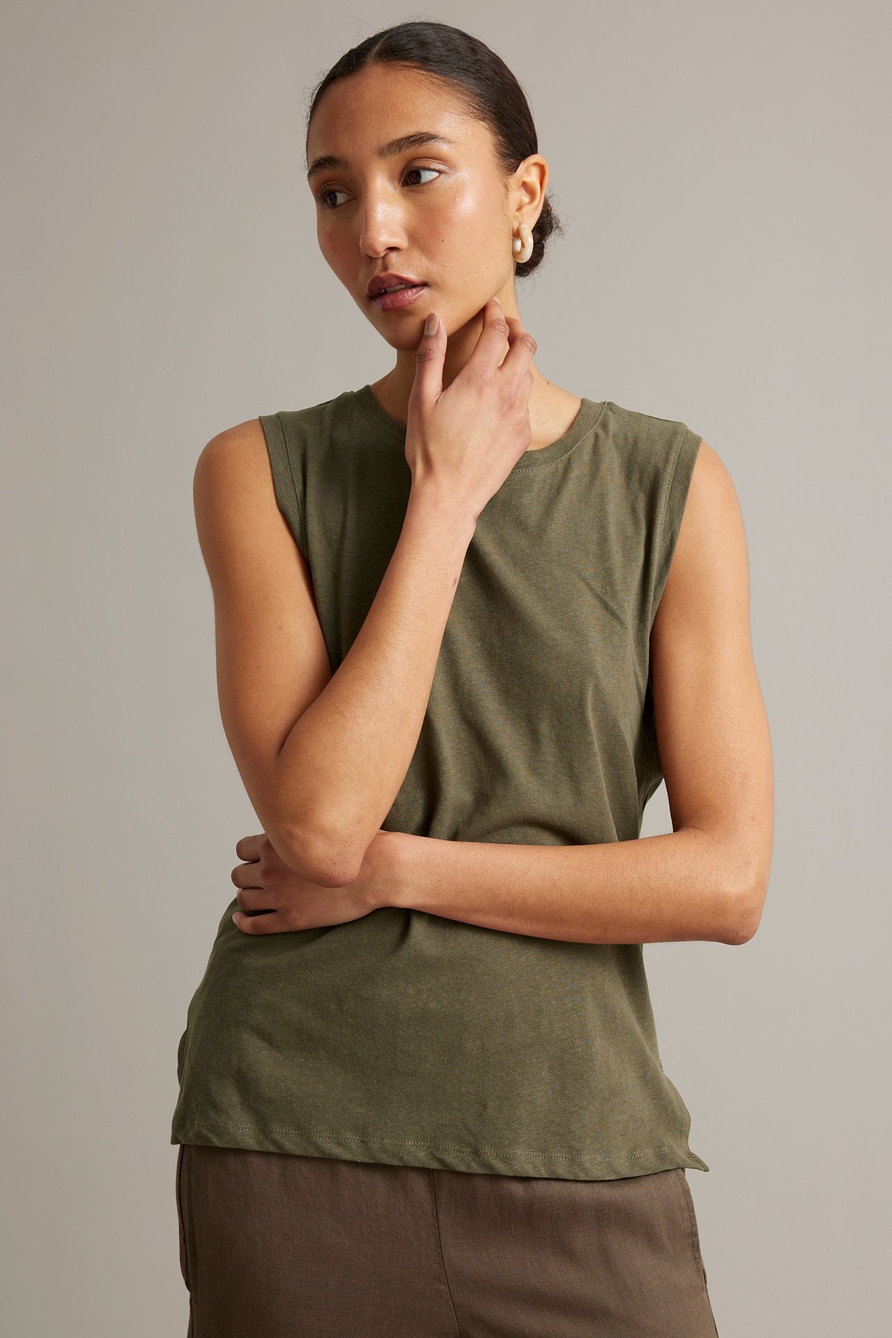 Framifrån: kvinna i khakigrön linneblandningstopp, bruna byxor och ljusa ringörhängen.