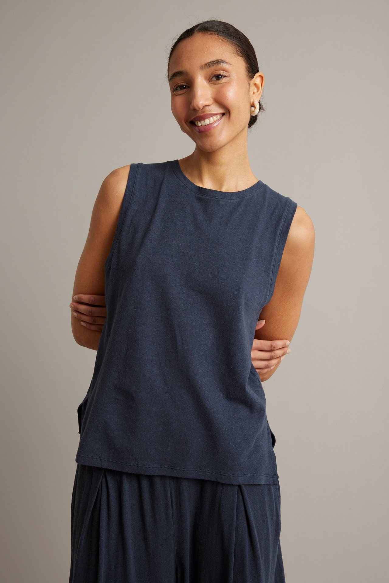 Frontvy av en kvinna i mörkblå tanktopp i linneblandning, matchande byxor och vita örhängen.