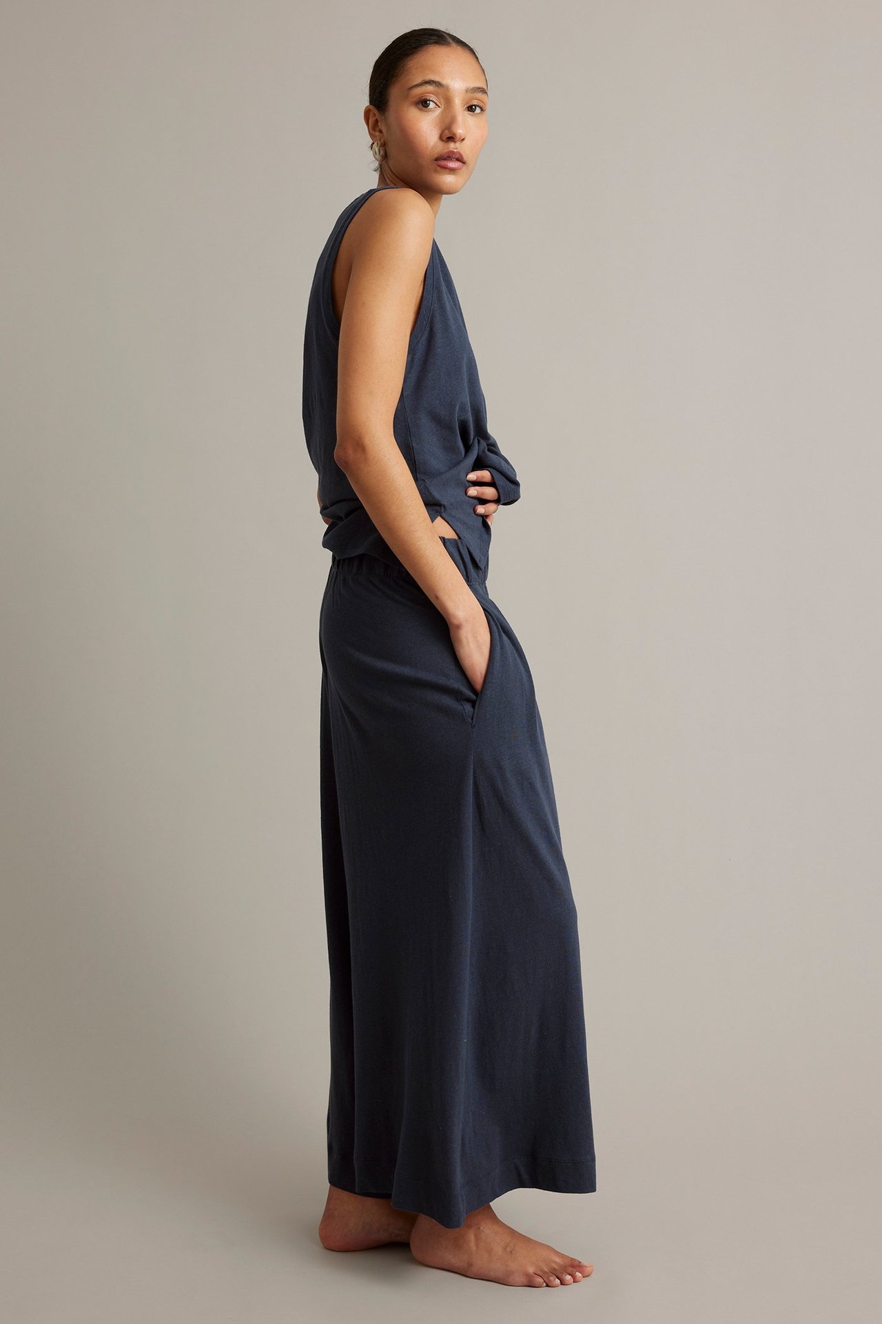 Kvinna i mörkblå linne-bomulls-tanktopp och matchande culottebyxor, handen i fickan, sidovy.