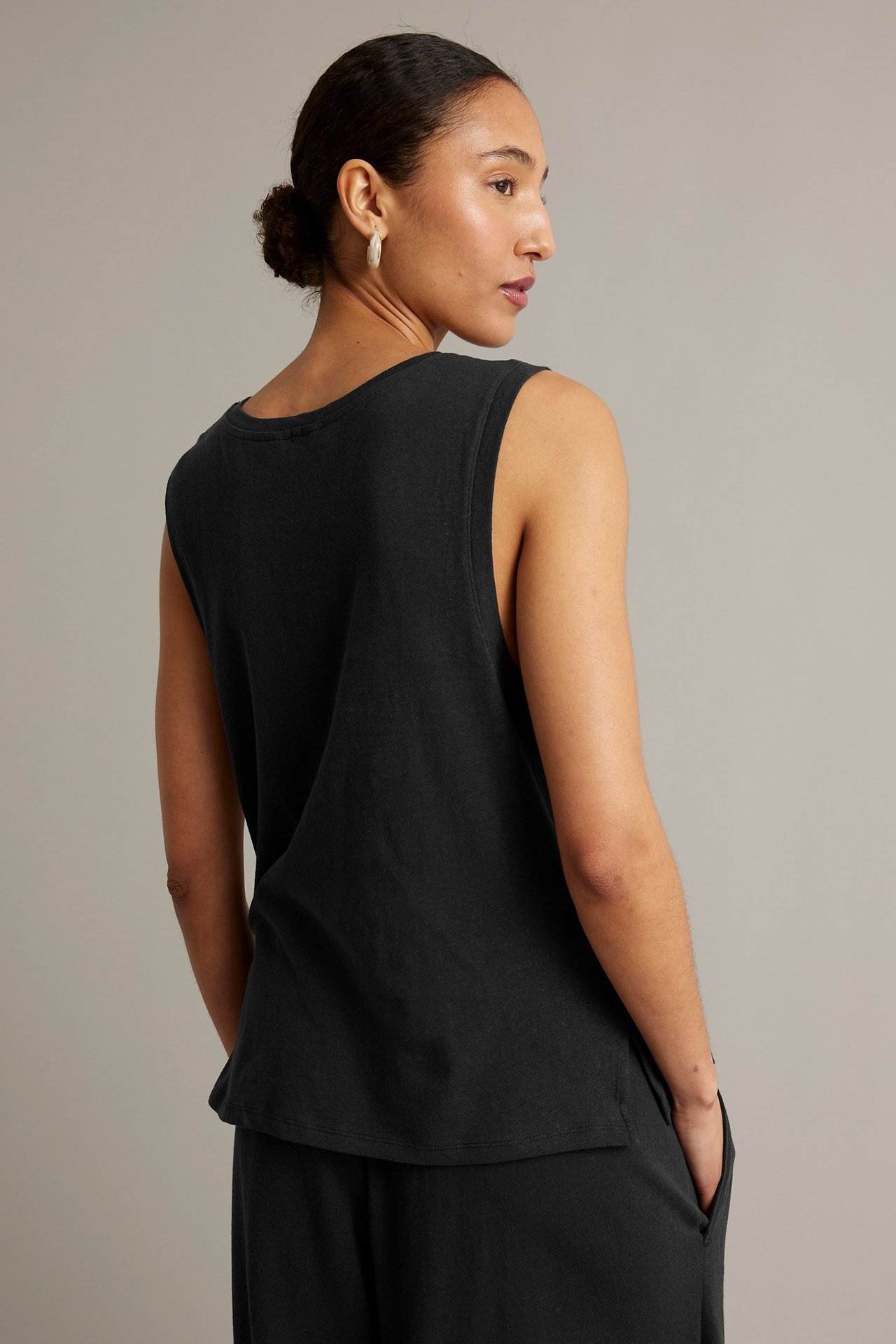Ryggvy av en kvinna i svart linneblandad tanktopp, stylad med svarta byxor och ljusa örhängen.