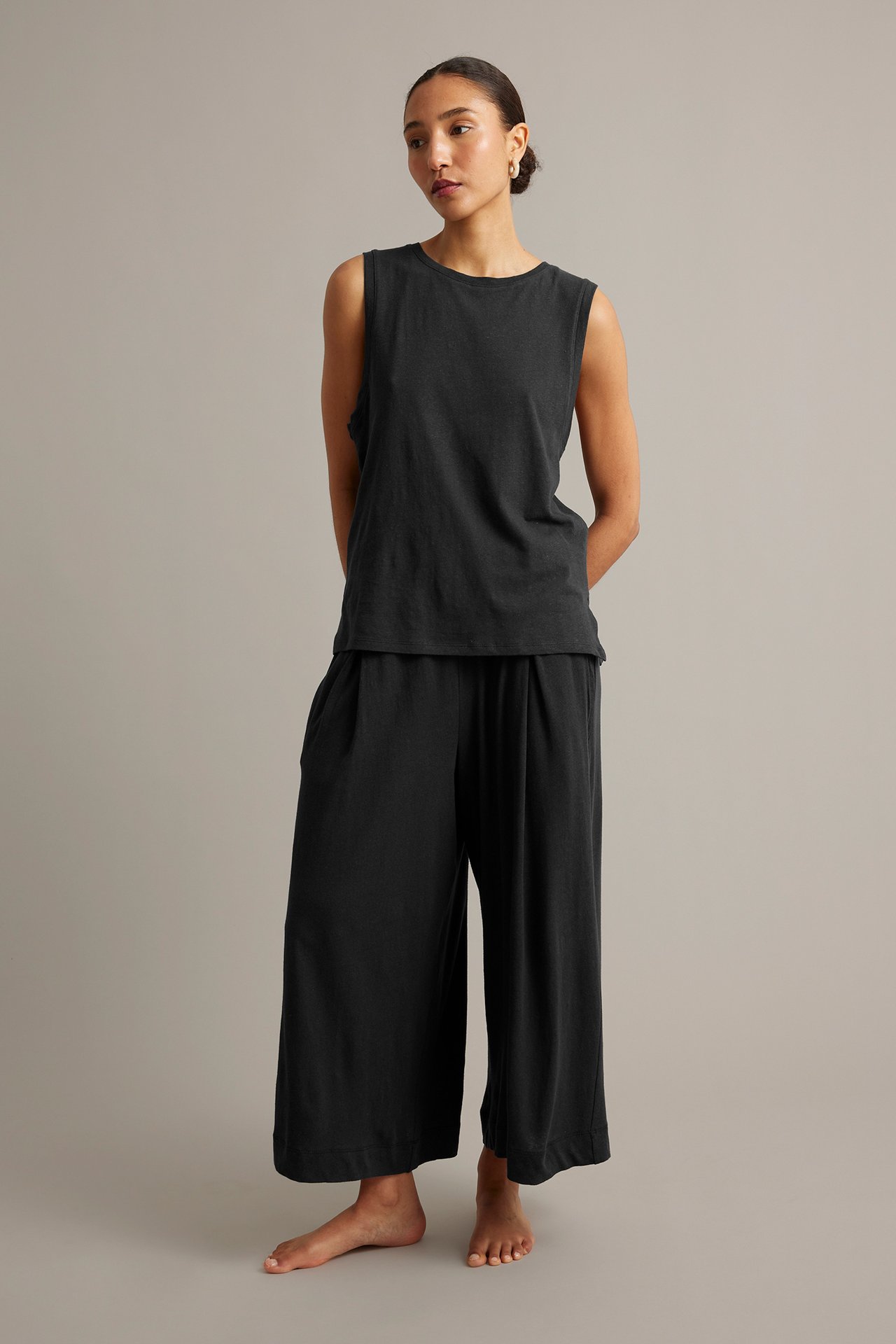 Framifrån, kvinna i svart linne- och bomullstopp med matchande svarta plisserade culottebyxor.