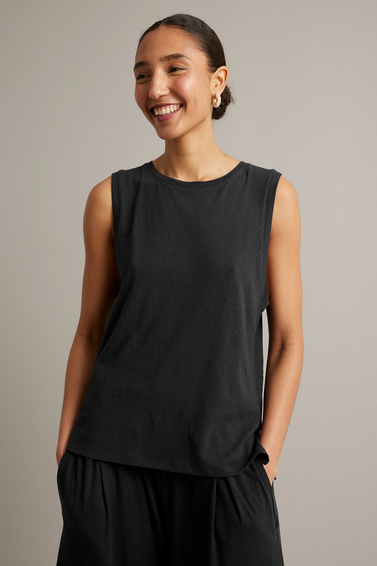 Frontvy av kvinna i svart tanktopp i bomull/linne, svarta culottebyxor och gräddfärgade ringörhängen.