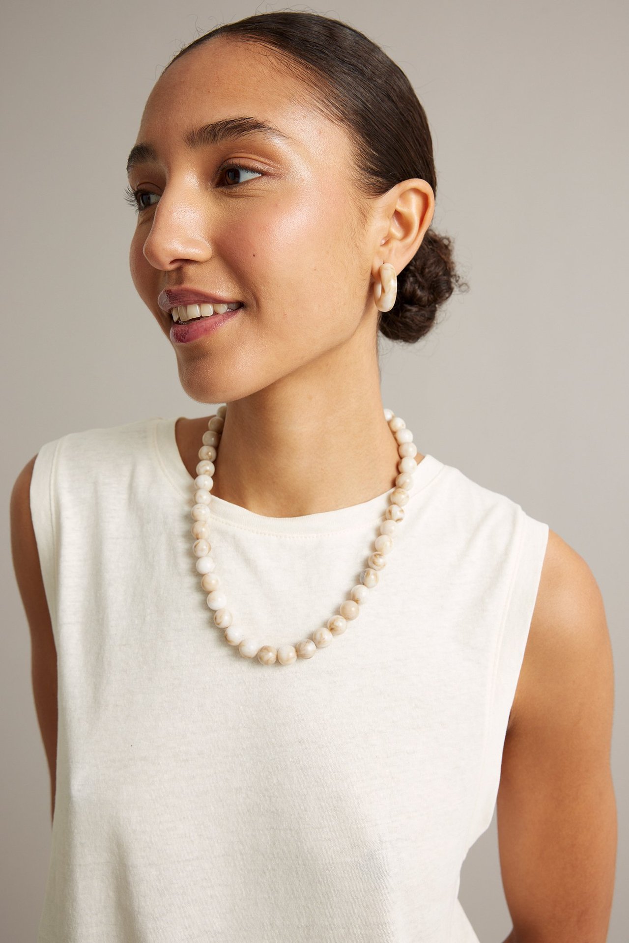 Sida vy av kvinna i vit linneblandad tanktopp, pärlhalsband och matchande örhängen.