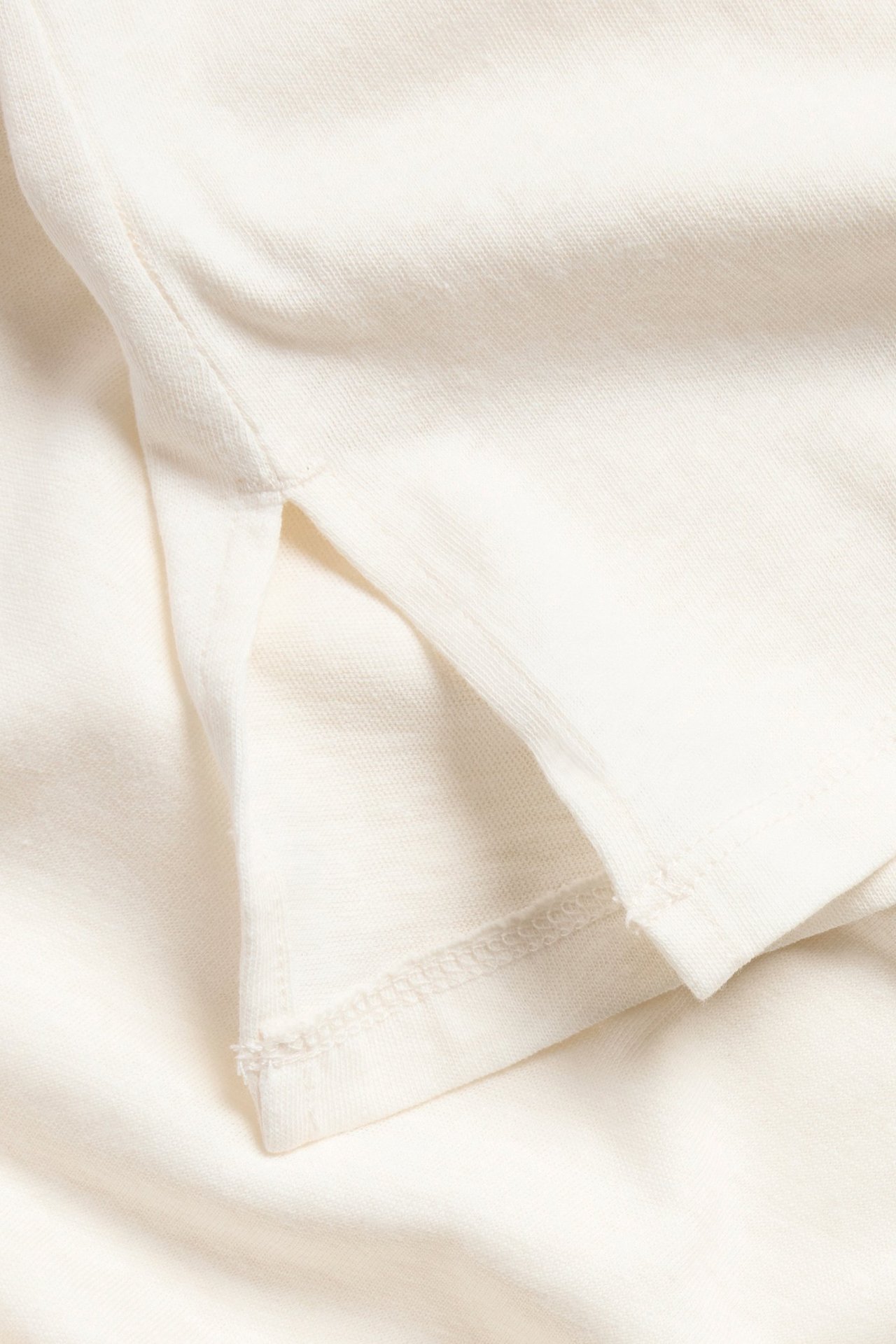 Zbliżenie białego topu z bawełny i lnu, pokazujące fakturę materiału i małe rozcięcie z boku.