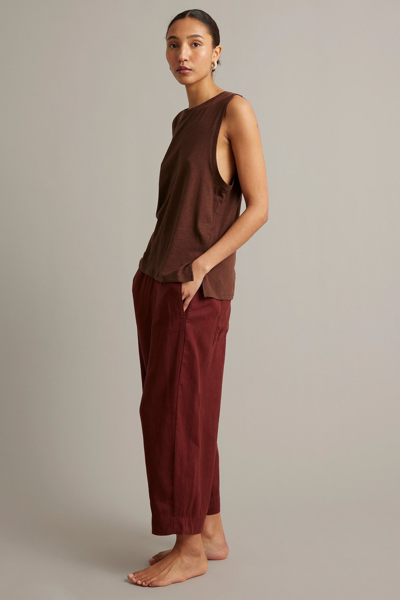 Sidovy av en kvinna i brun tanktopp i linneblandning och lösa vinröda culottebyxor.