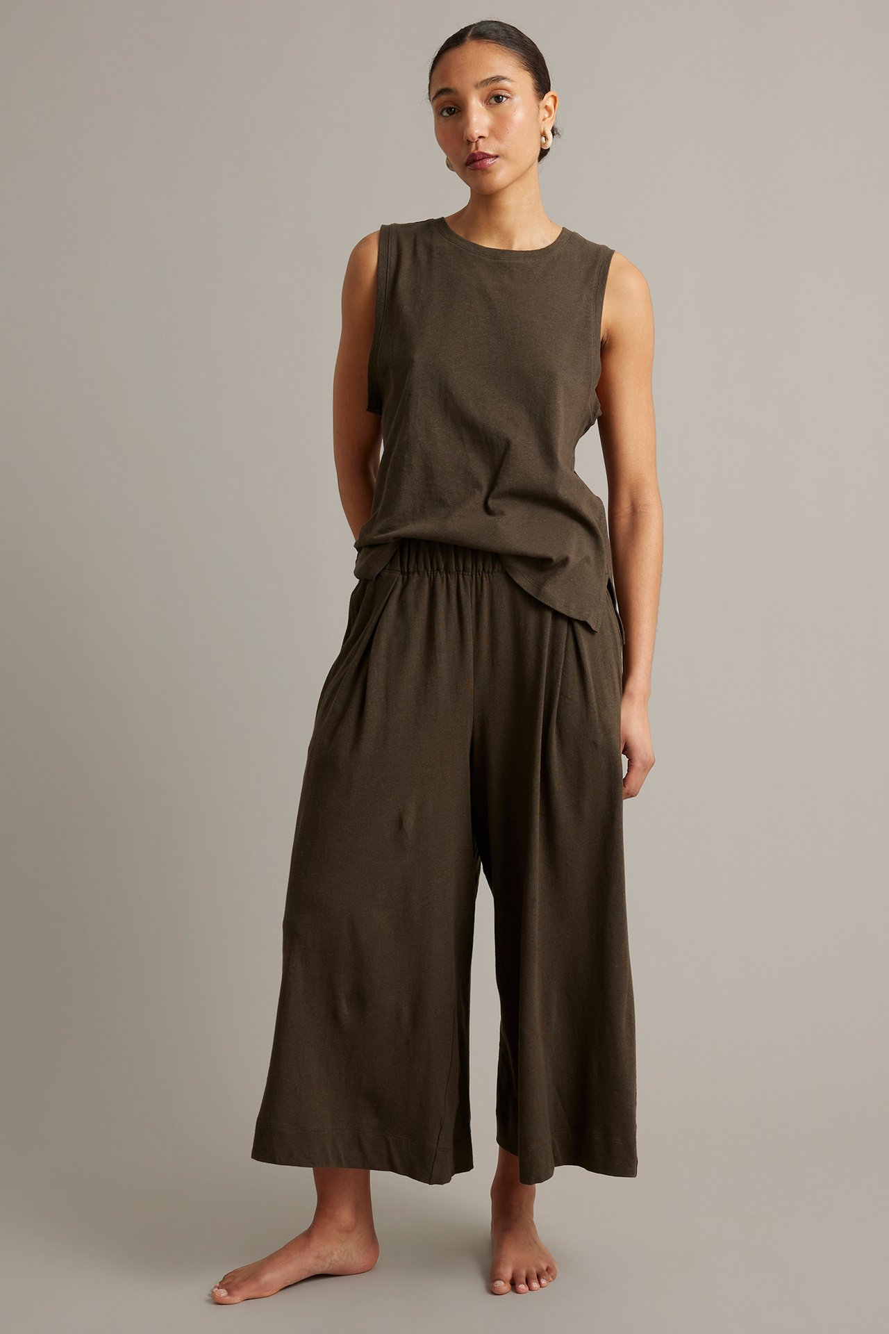 Edestä näkymä naisesta ruskeissa leveälahkeisissa culotte-housuissa laskoksilla ja yhteensopivassa hihattomassa paidassa.