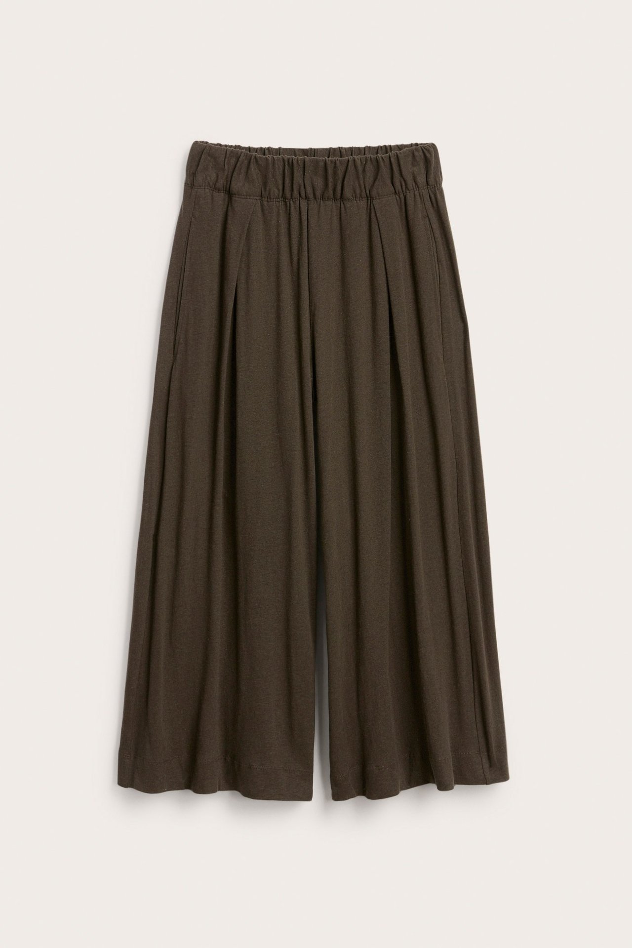 Framifrån bild av enfärgade mörkbruna vida culottebyxor med veck och resår i midjan.
