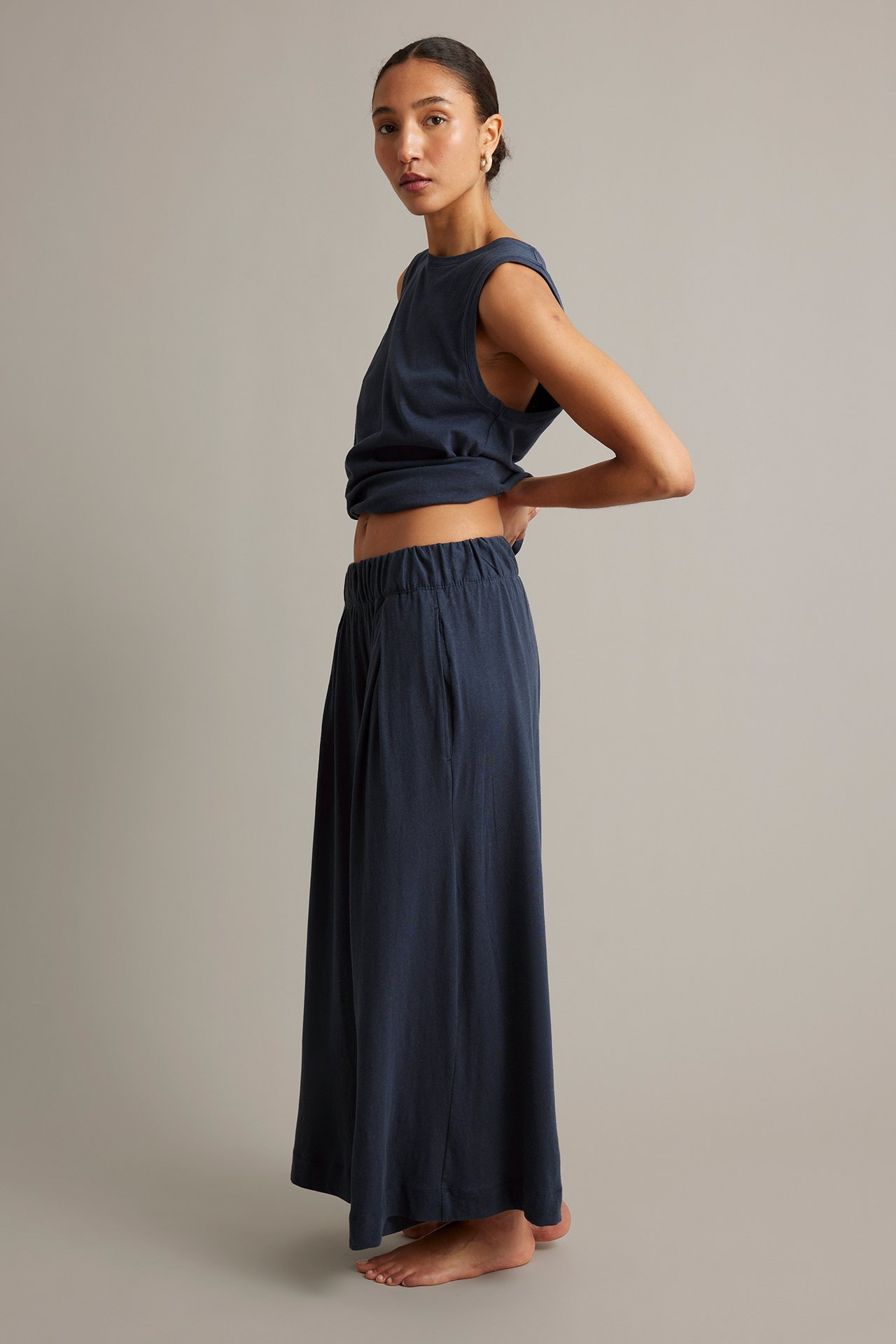 Sidovy av en kvinna i mörkblå vida culottebyxor med resår i midjan och matchande ärmlös topp.