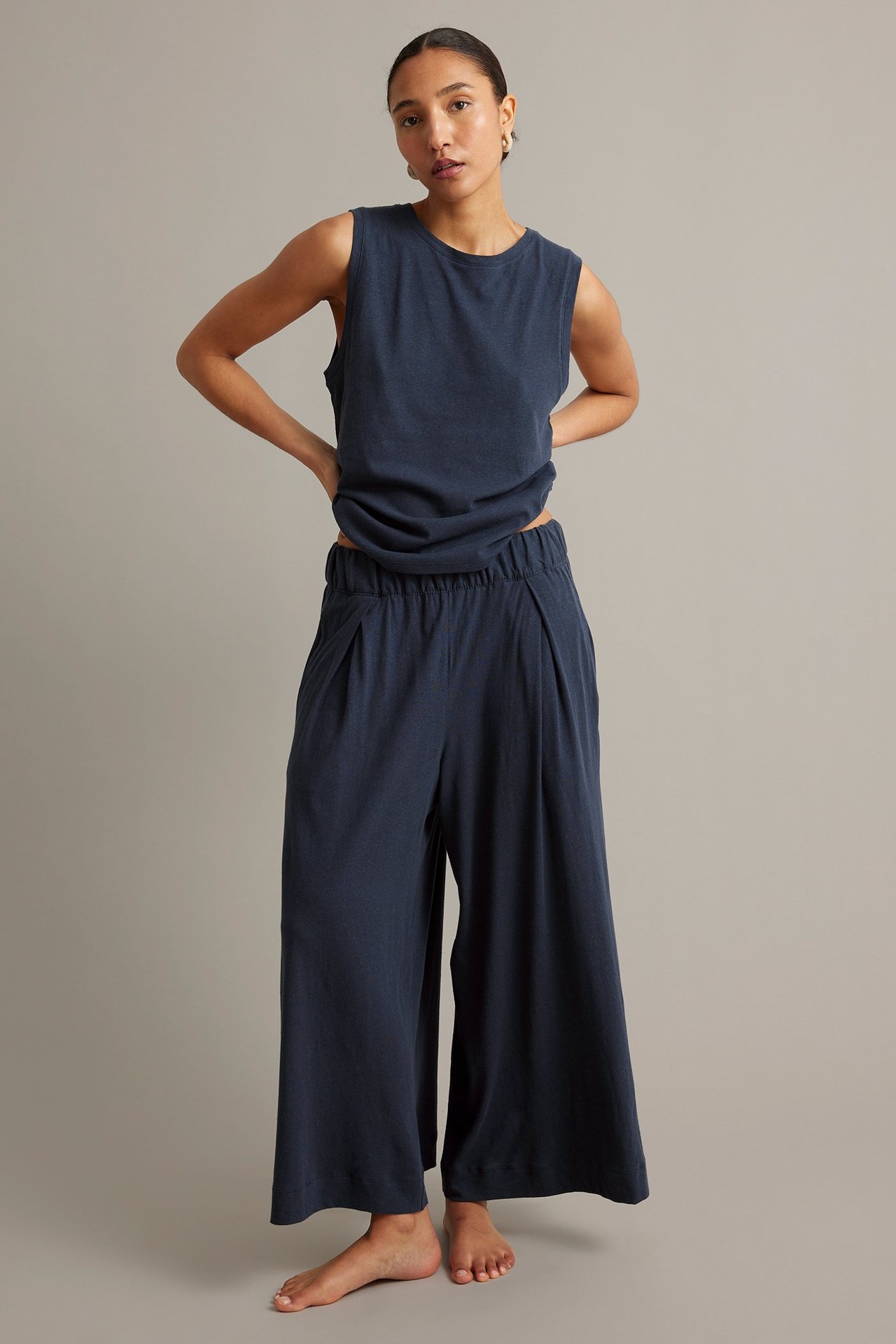 Frontvy: Kvinna i mörkblå vida byxor i bomull-linne med resår i midjan och matchande linne.