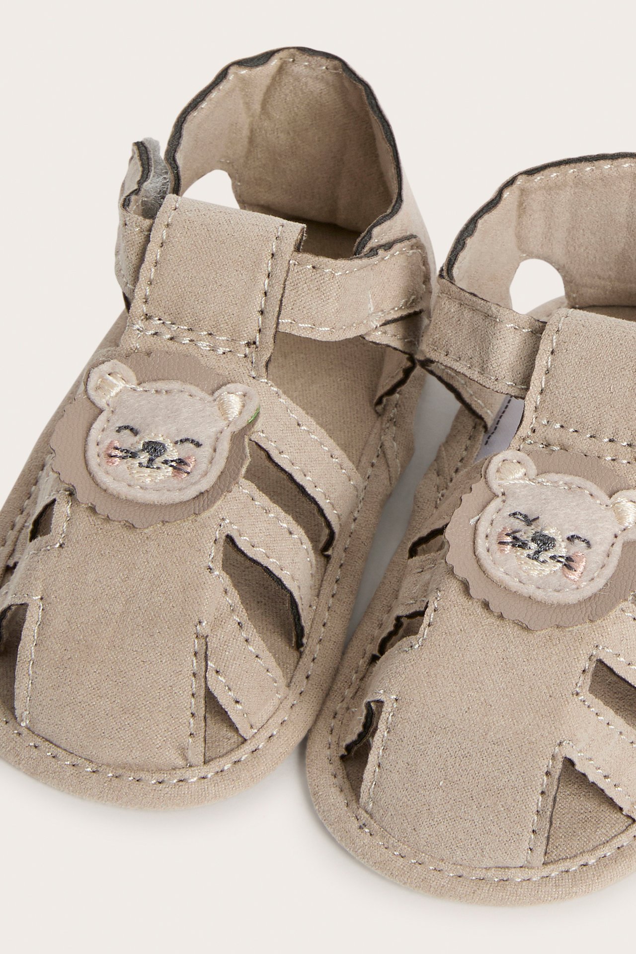 Nærbilde av et par beige babysandaler med løveapplikasjon og borrelås.