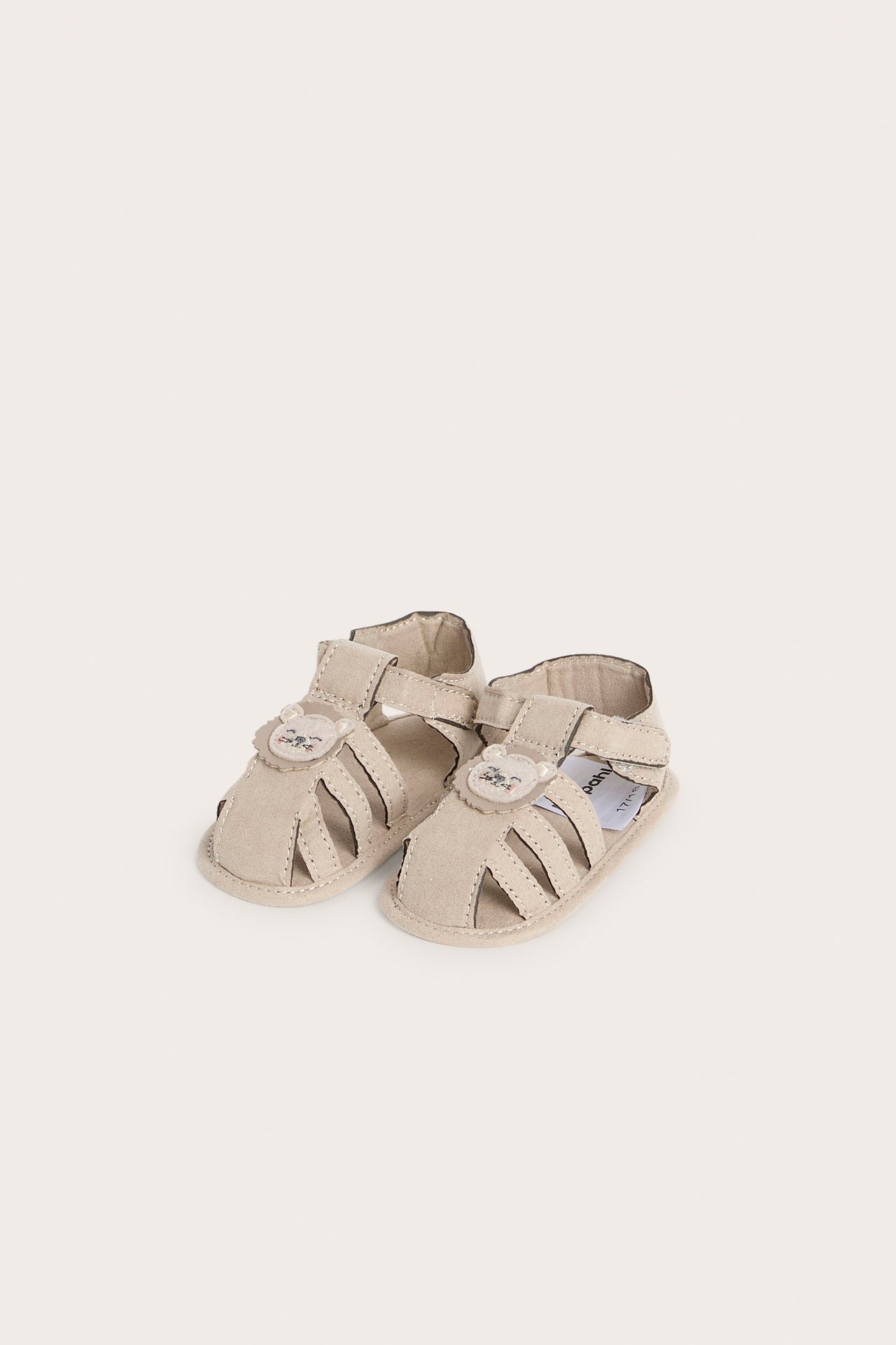 Frontvisning av beige babysandaler med løveapplikasjoner og borrelåsstropper.