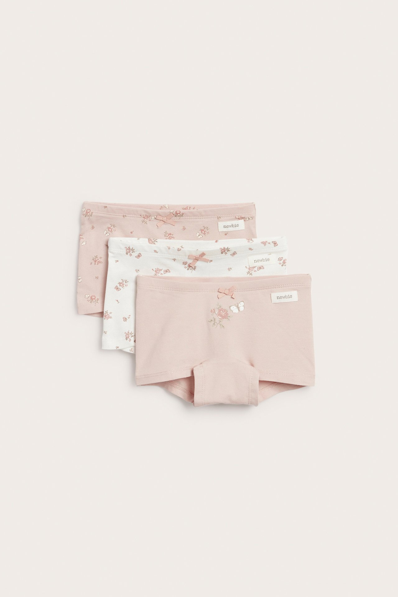 Widok z przodu dziecięcych różowych bokserek z różami i motylami, a także białe i jasnoróżowe pary w kwiaty.
