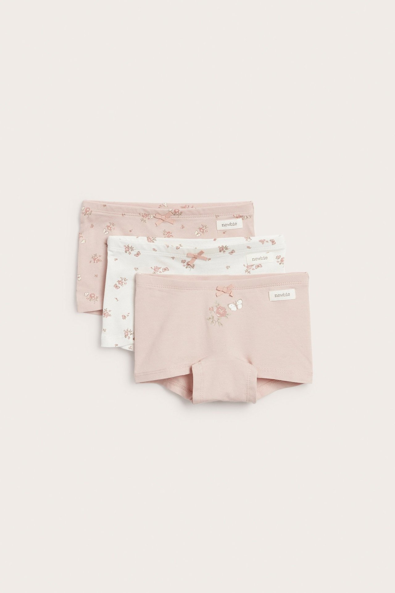 Widok z przodu dziecięcych różowych bokserek z różami i motylami, a także białe i jasnoróżowe pary w kwiaty.