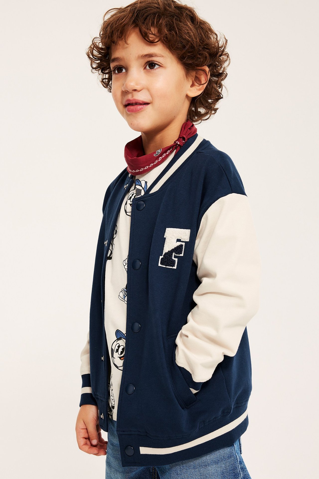 Widok z przodu: Dziecko nosi granatową, kremową bawełnianą kurtkę bejsbolową z zatrzaskami i naszywką 'F'.