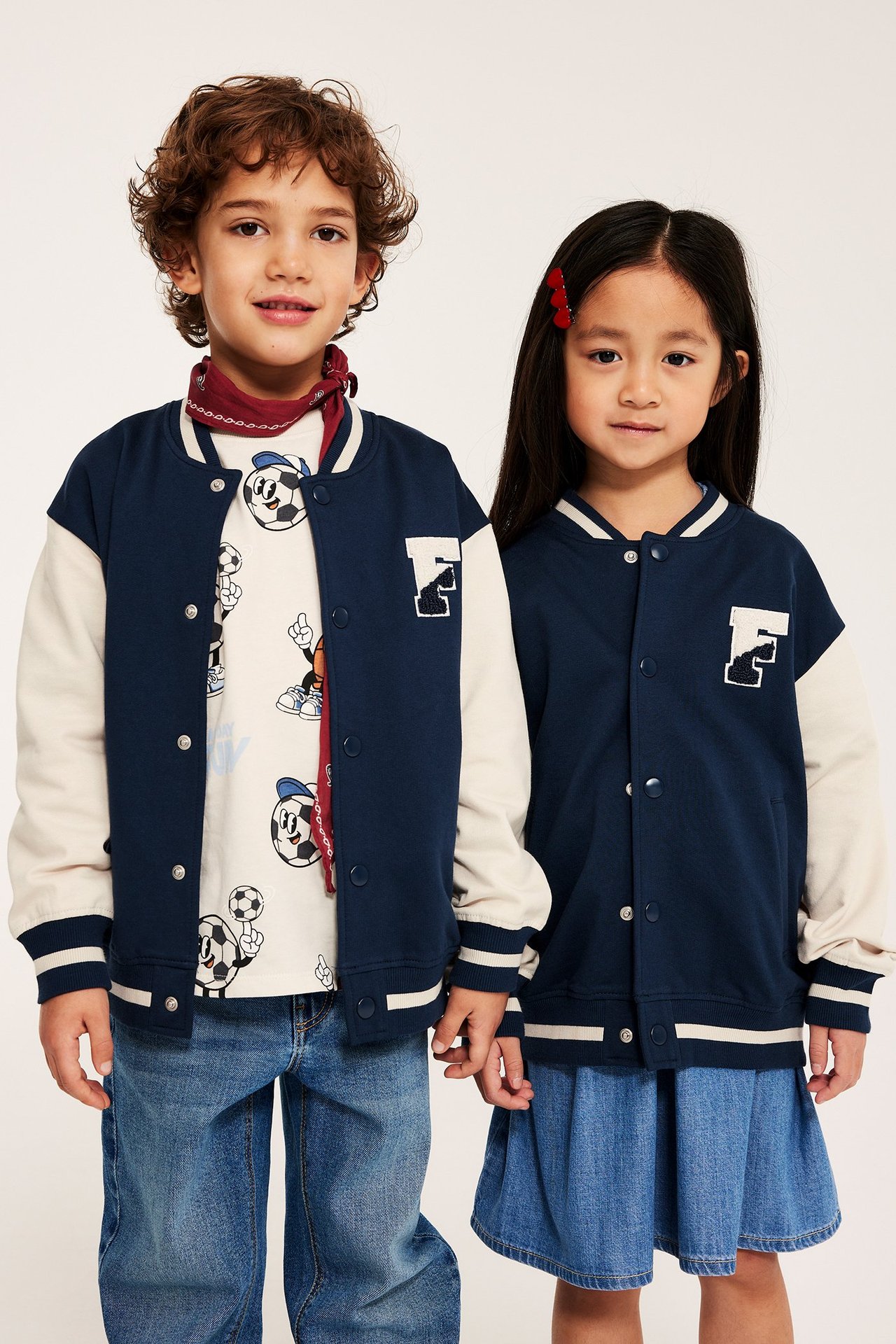 Widok z przodu: dwoje dzieci w granatowych kurtkach bejsbolówkach, z beżowymi rękawami i białą naszywką 'F'.