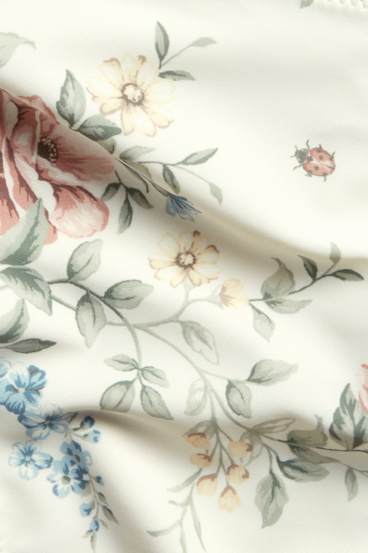 Nærbilde av offwhite bikinitruse-stoff med blomstermønster og en liten marihøne.