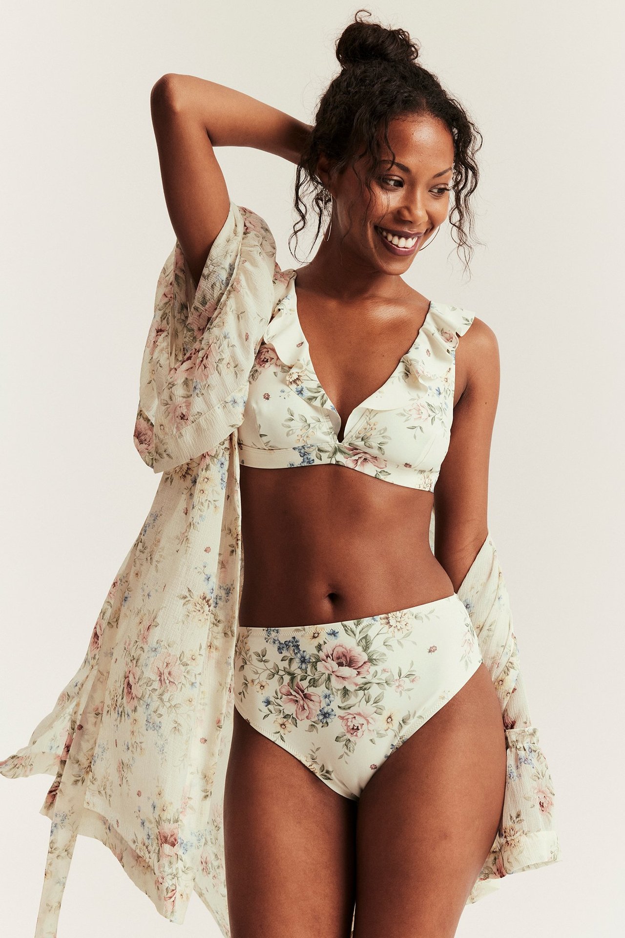 Smilende kvinne, forfra, i offwhite blomstret høy midje bikinitruse, matchende topp og kimono.