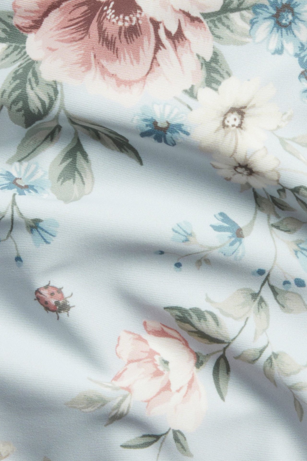 Nærbilde av lys blå bikinitrusestoff med rosa og blått blomstermønster og en marihøne.