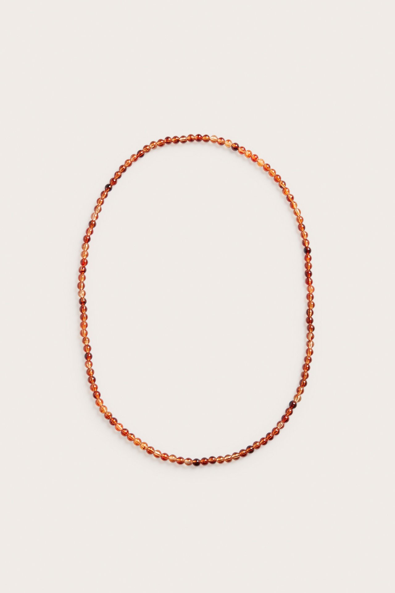 Närbild på långt halsband med bärnstensfärgade plastpärlor, lagt i en oval.