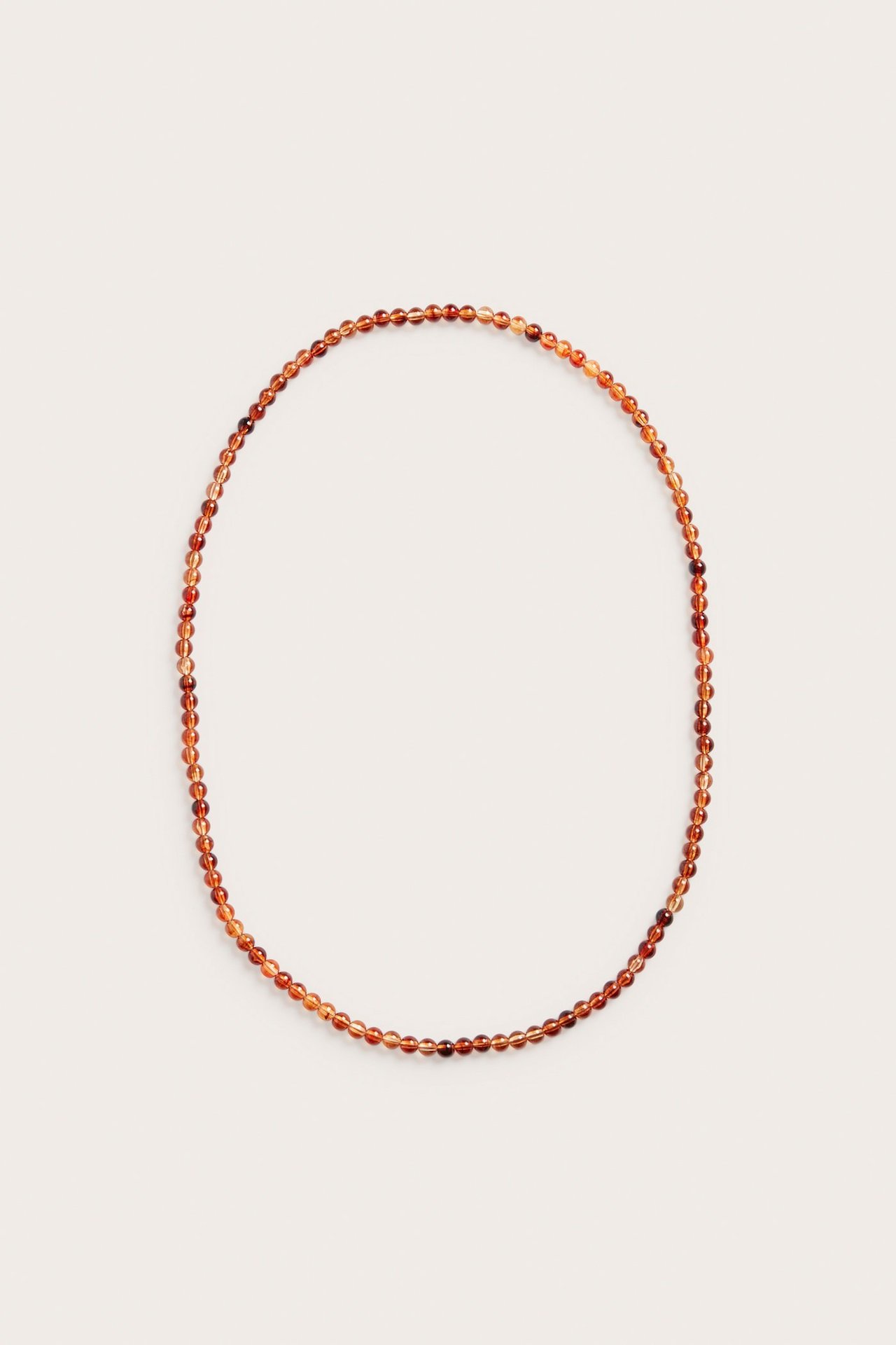 Nærbilde av langt halskjede med ravfargede plastperler, lagt i en oval form.