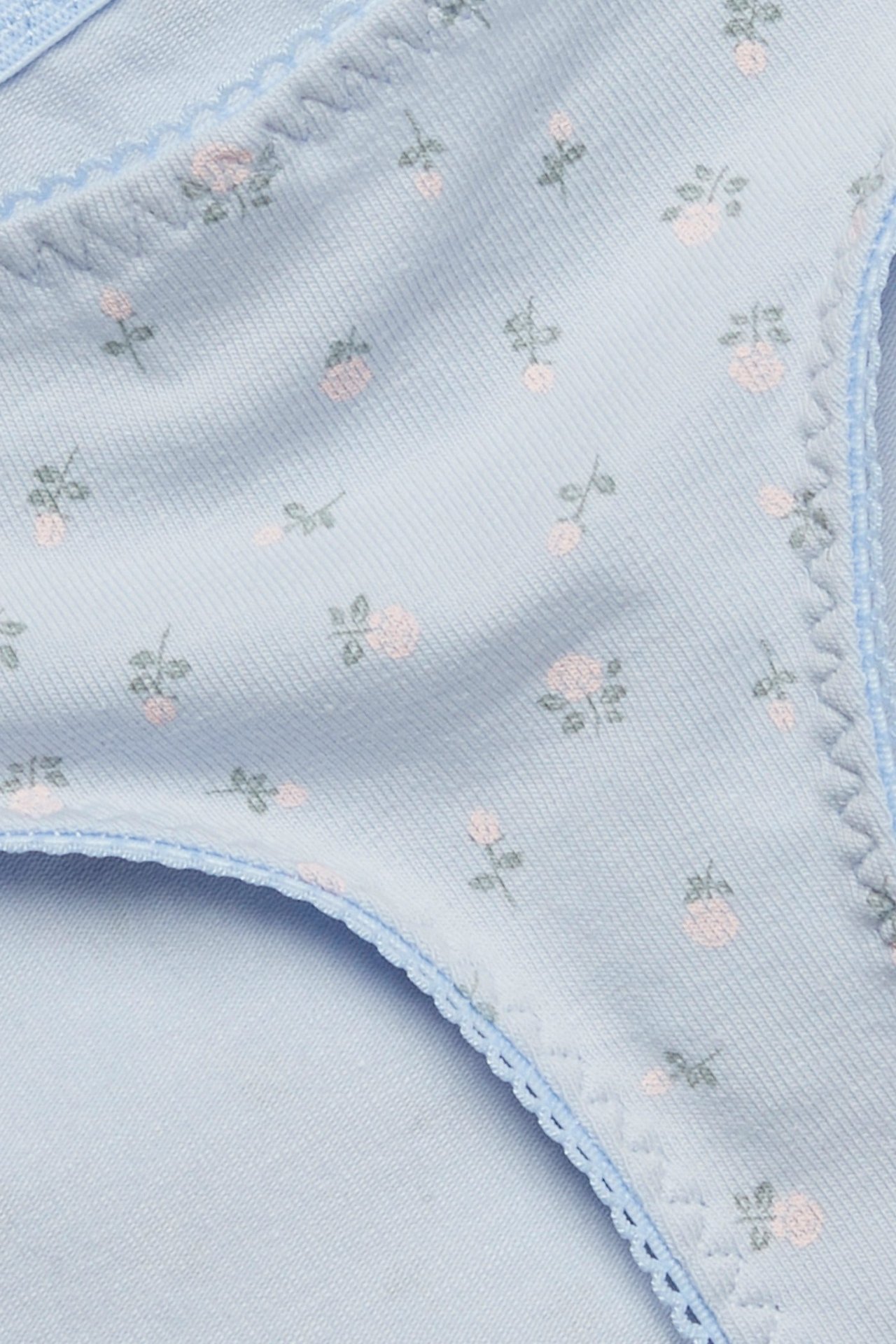 Lähikuva vaaleansinisistä puuvillastringeistä pienellä vaaleanpunaisella kukkakuviolla ja picot-reunuksella.
