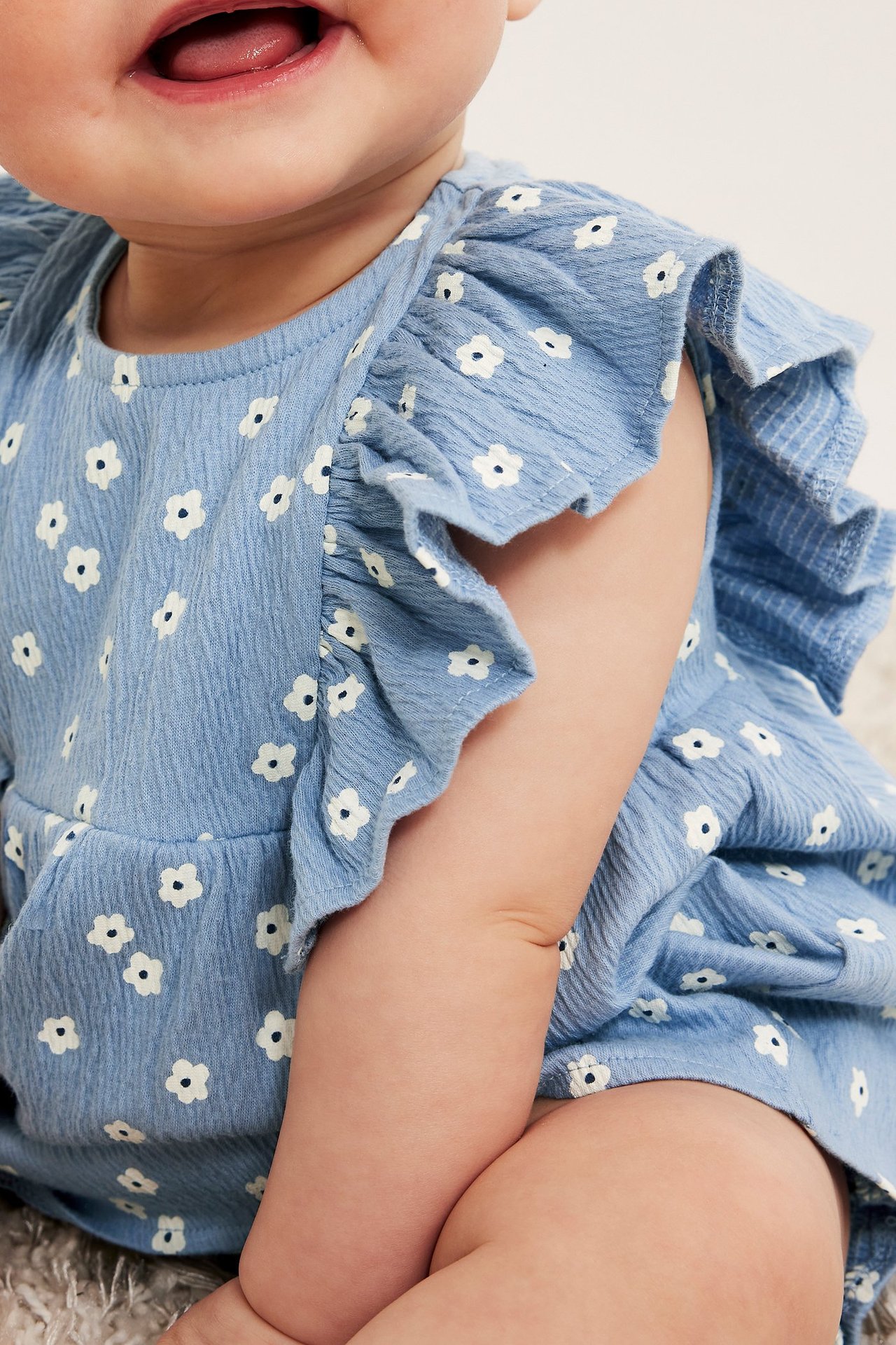 Zbliżenie dziecka w jasnoniebieskim kwiecistym topie z krepy bawełnianej z falbanami, część zestawu.