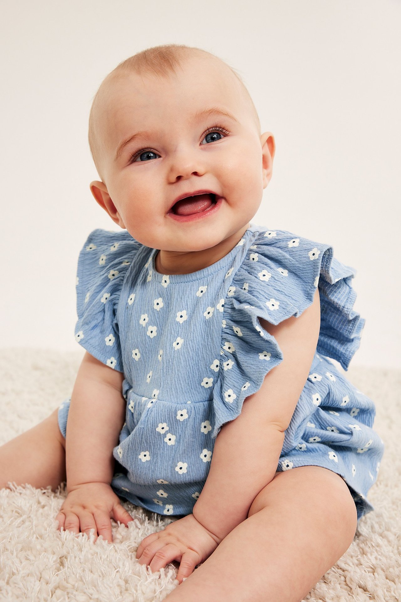 Widok z przodu radosnego dziecka w jasnoniebieskim, kwiecistym zestawie krepowym z falbankowym topem i pasującymi bloomersami.