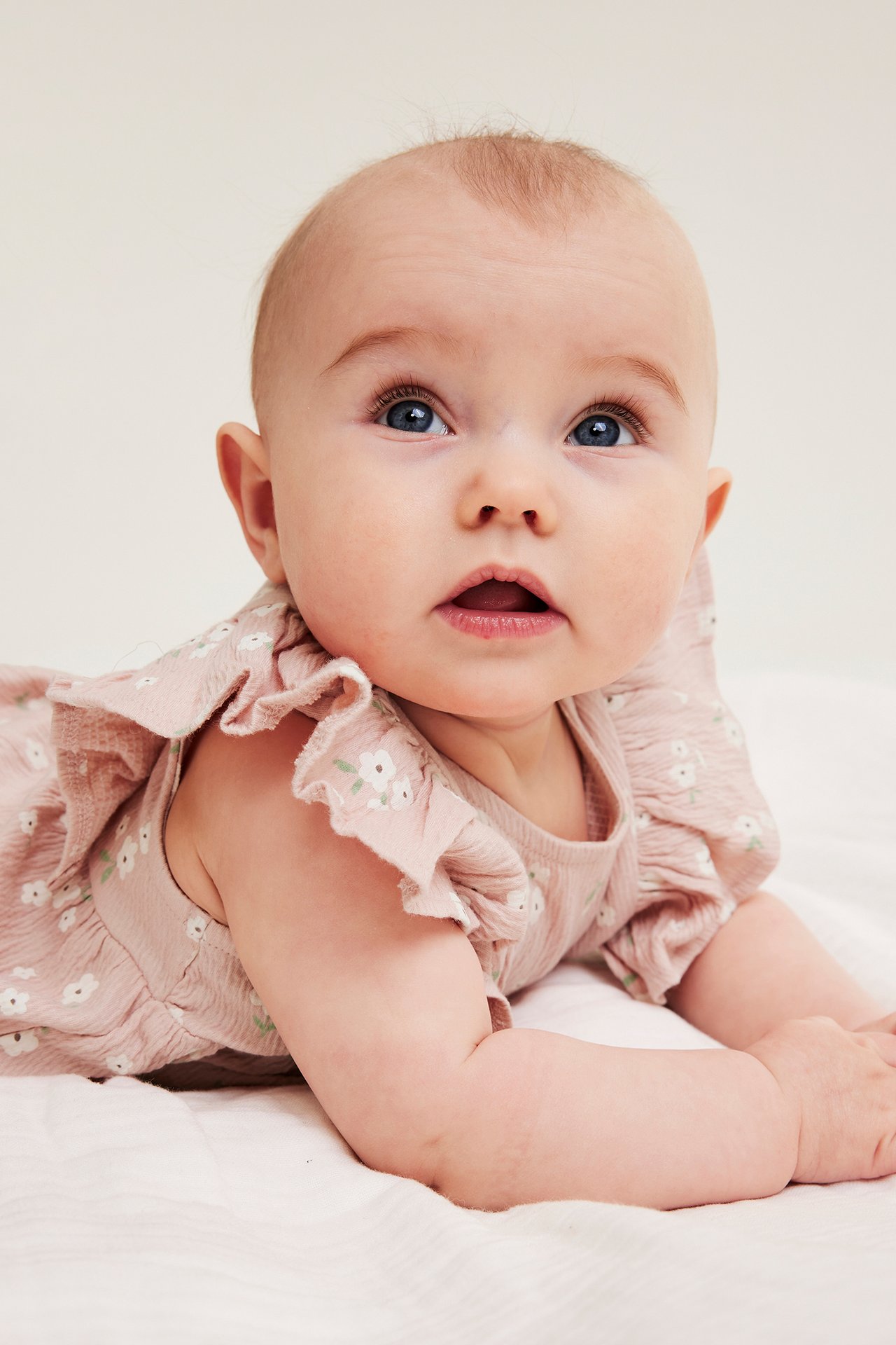 Lähikuva vauvasta, jolla on vaaleanpunainen kukkakuvioinen puuvillakreppitoppi röyhelöhihoilla.