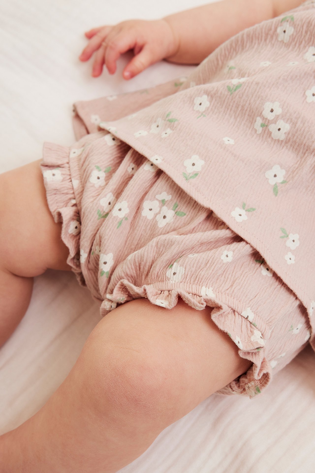 Nærbilde av en baby i et rosa blomstret sett av bomullskrepp, med topp og volangbloomers.