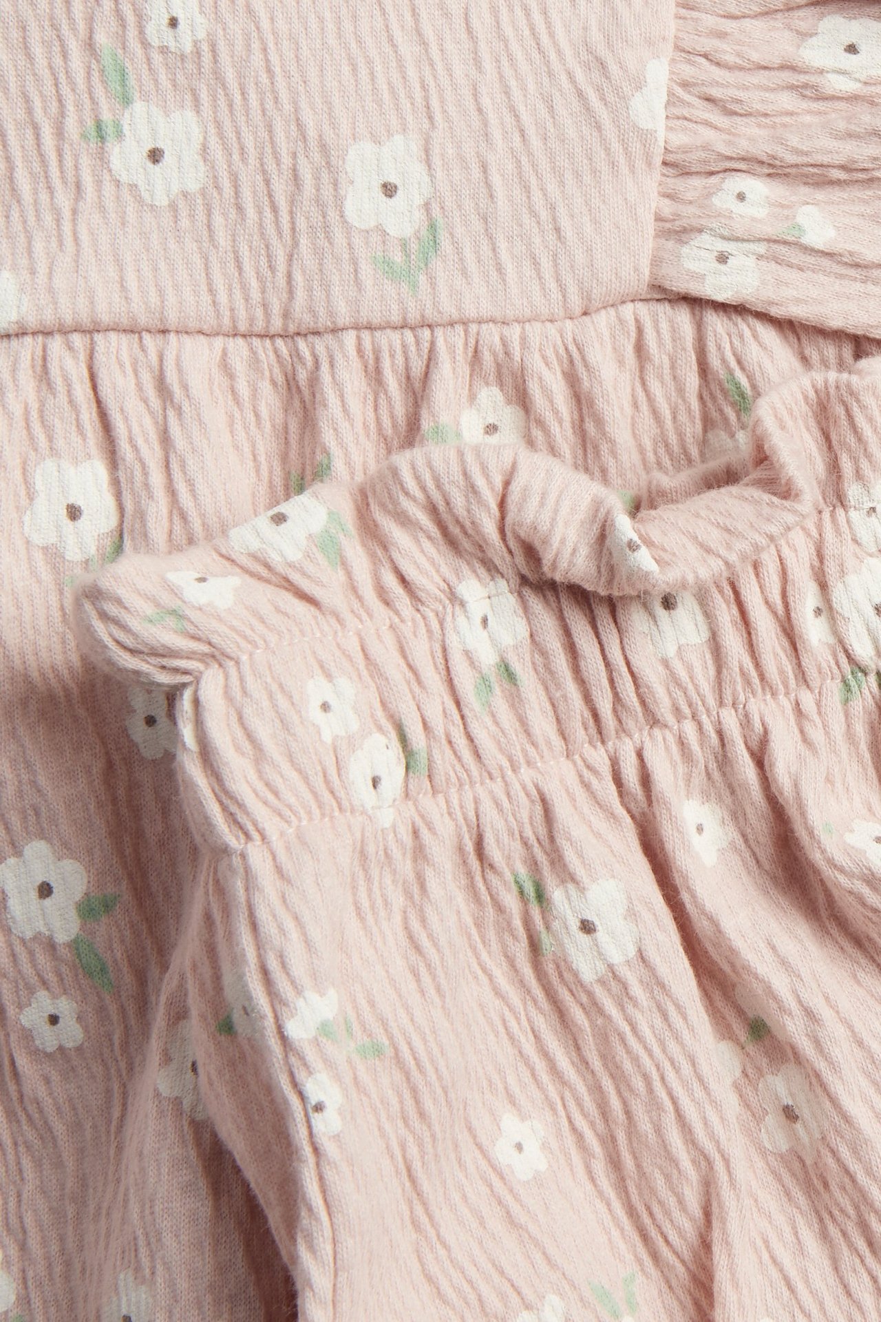 Zbliżenie różowego kompletu niemowlęcego w kwiaty z marszczoną bluzką i bloomersami z bawełnianej krepy.