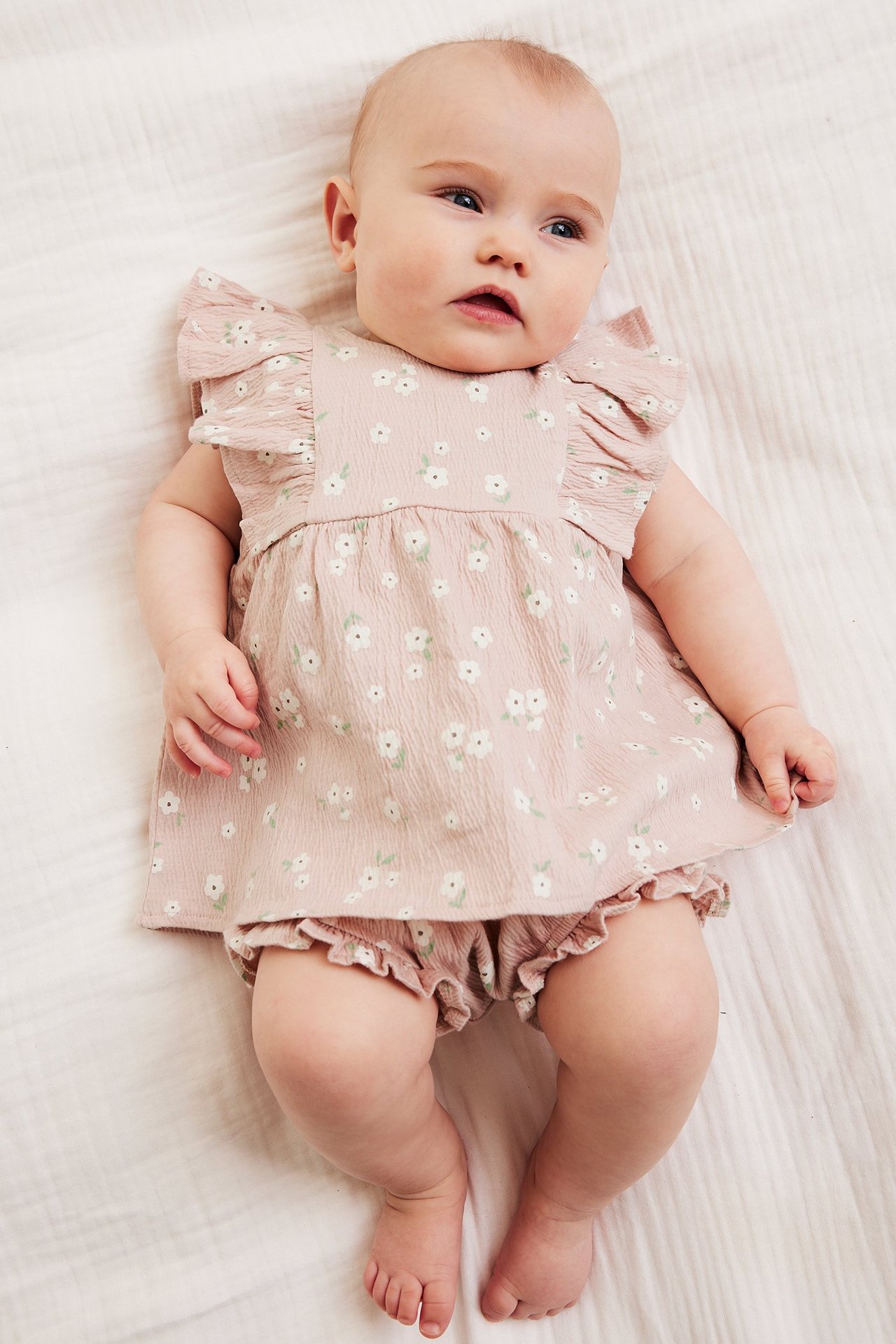 Topputsikt av en baby i et rosa blomstrete kreppsett med volangermet topp og matchende bloomers.