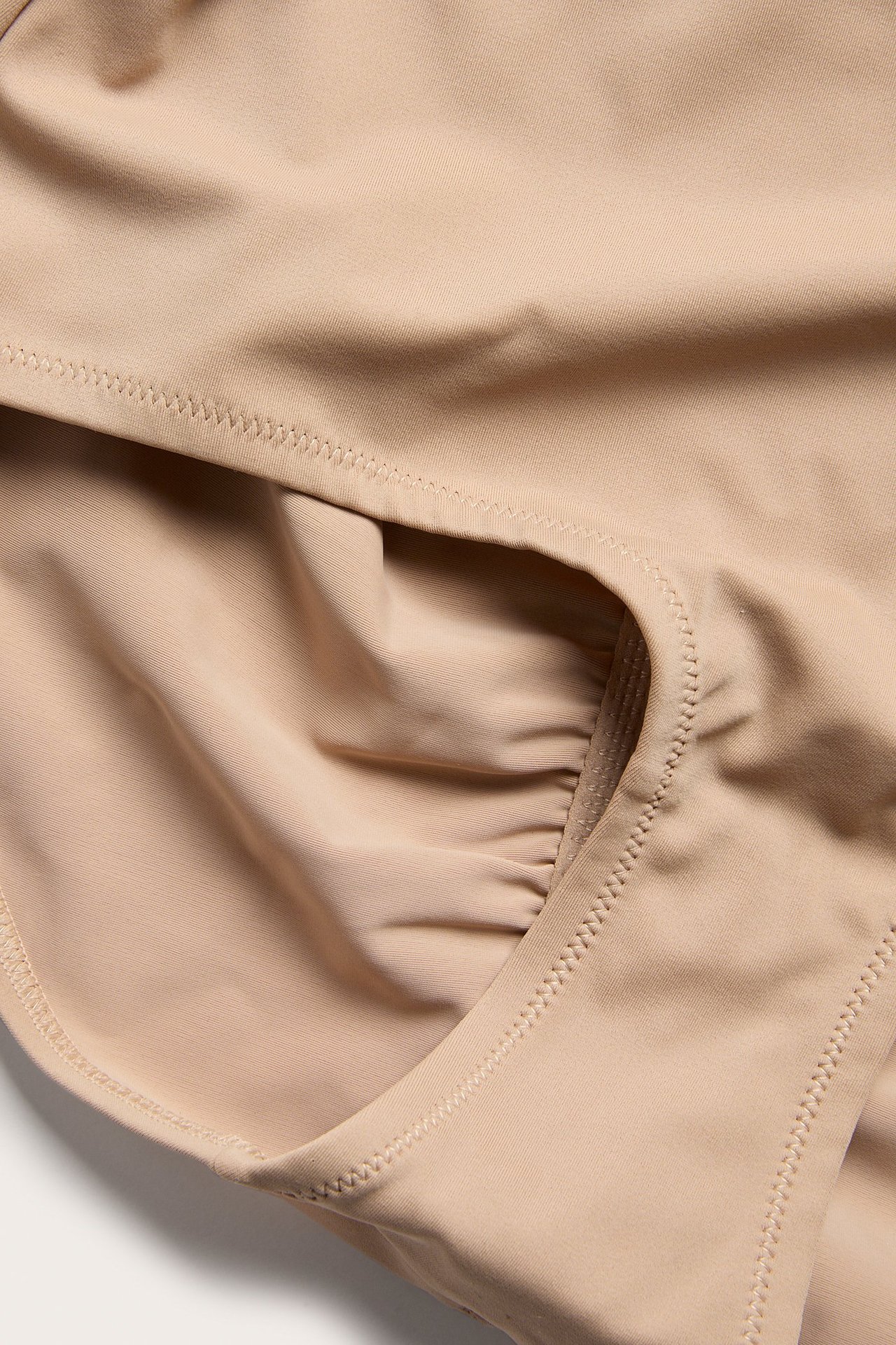 Zbliżenie na gładkie brązowe figi modelujące typu hipster z wysokim stanem i subtelnym marszczeniem.