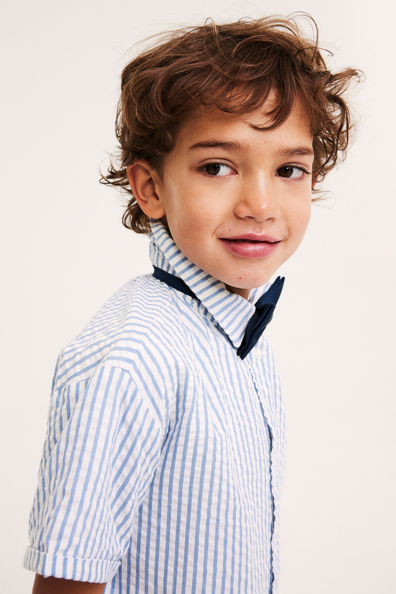 Zbliżenie z boku na dziecko w granatowej satynowej muszce założonej na jasnoniebieską koszulę w paski.