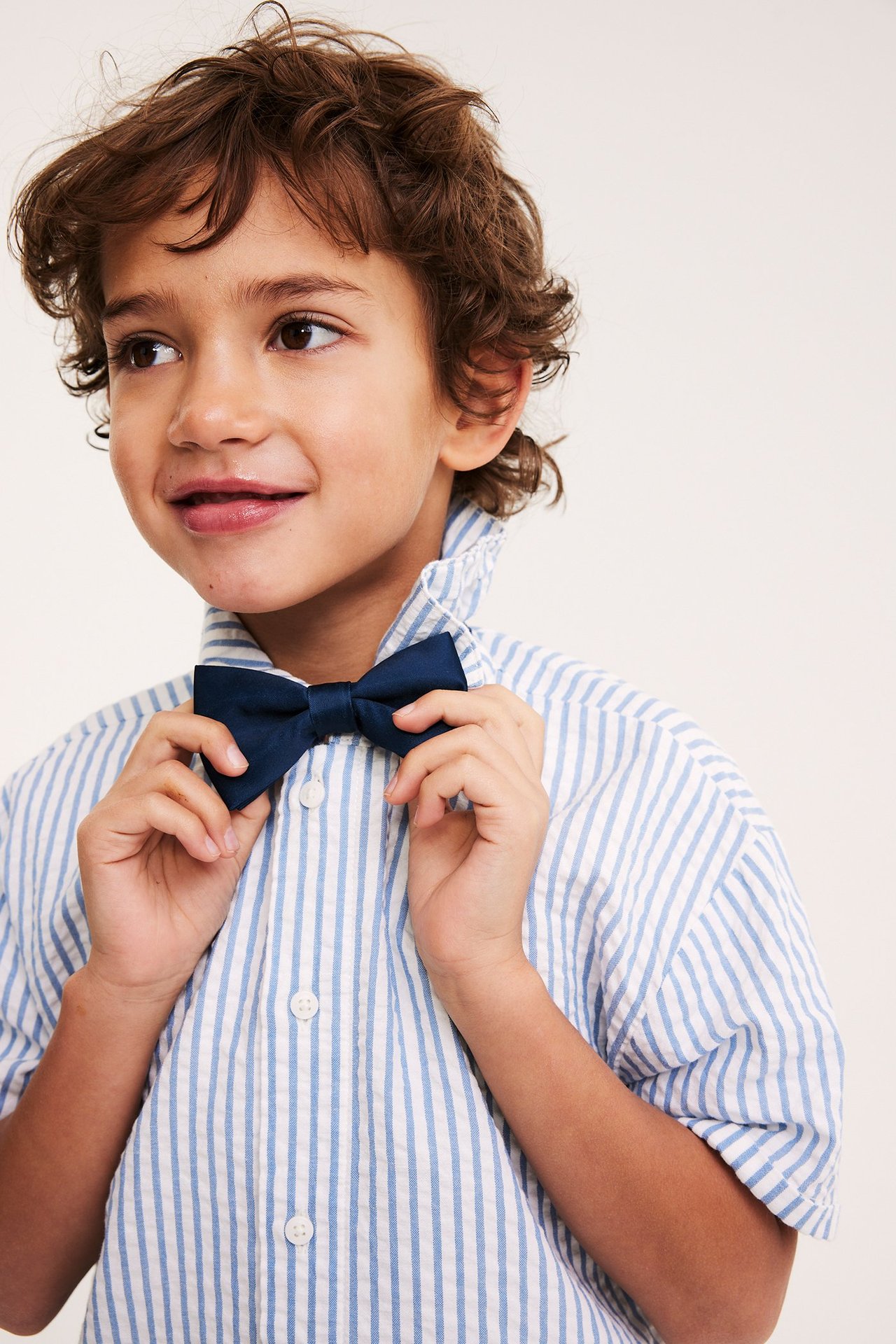 Zbliżenie: dziecko poprawia granatową satynową muszkę na koszuli w paski.