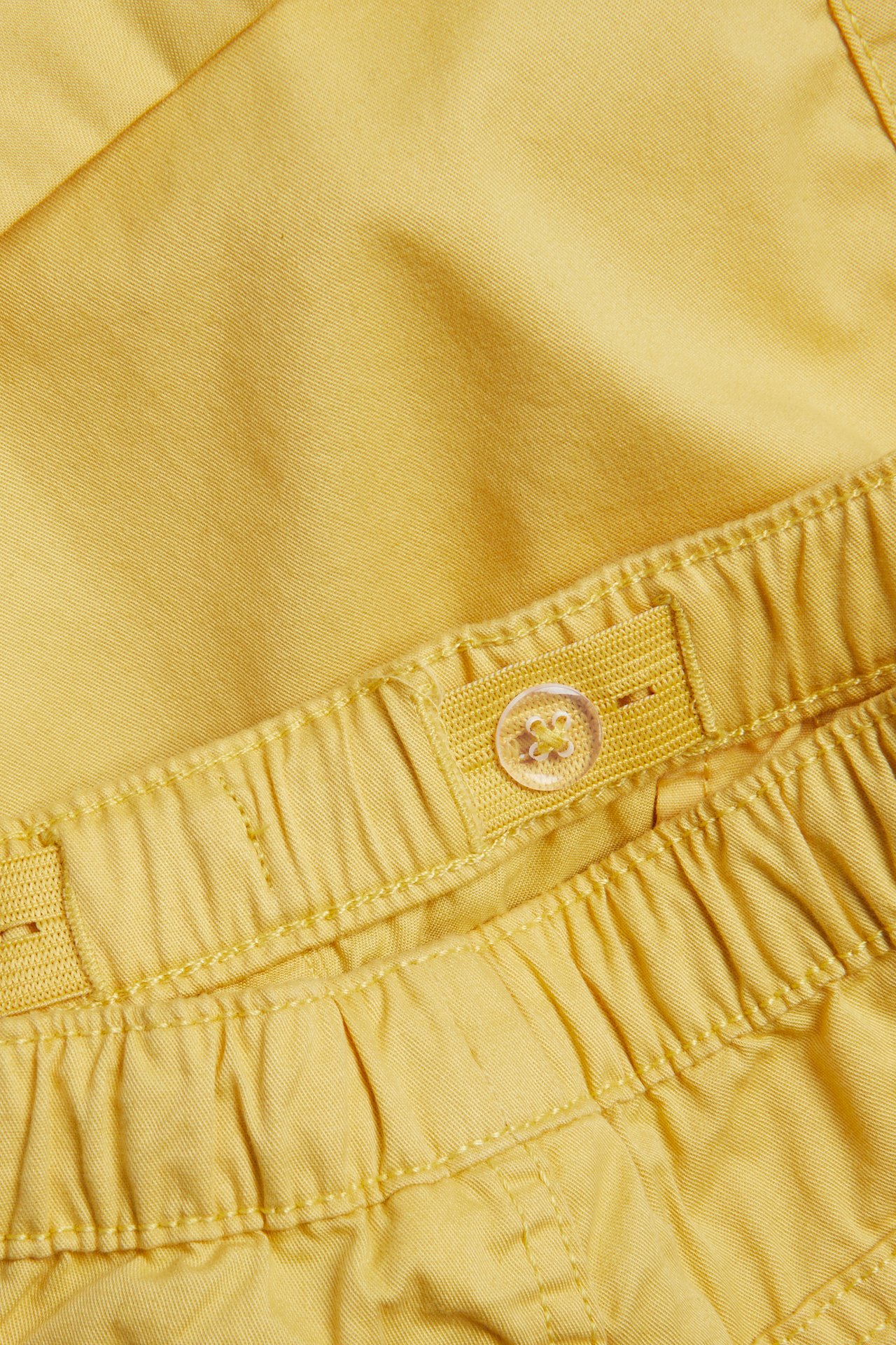 Zbliżenie na pas żółtych szortów dziecięcych, z elastyczną regulacją i przezroczystym guzikiem.