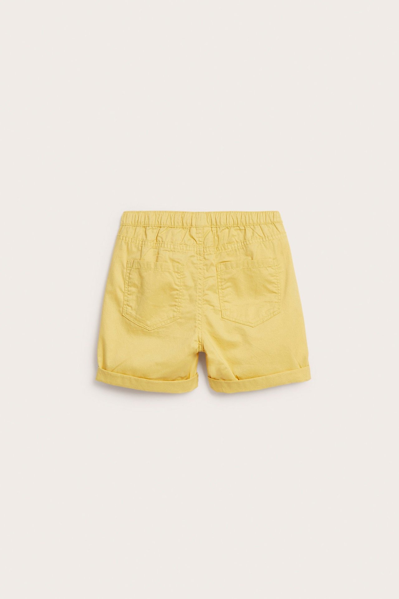Widok z tyłu: Dziecięce gładkie żółte szorty z diagonalu bawełnianego, z elastyczną talią i podwiniętymi nogawkami.
