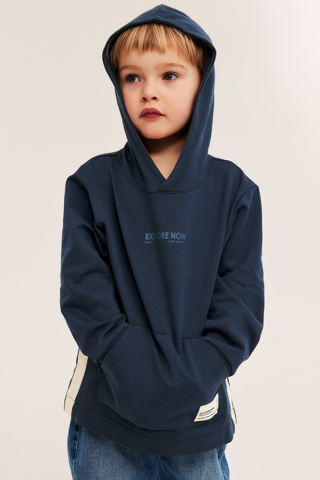 Przód: dziecko w granatowej bawełnianej bluzie z kapturem, nadrukiem, kieszenią kangurką i jasnymi panelami bocznymi.