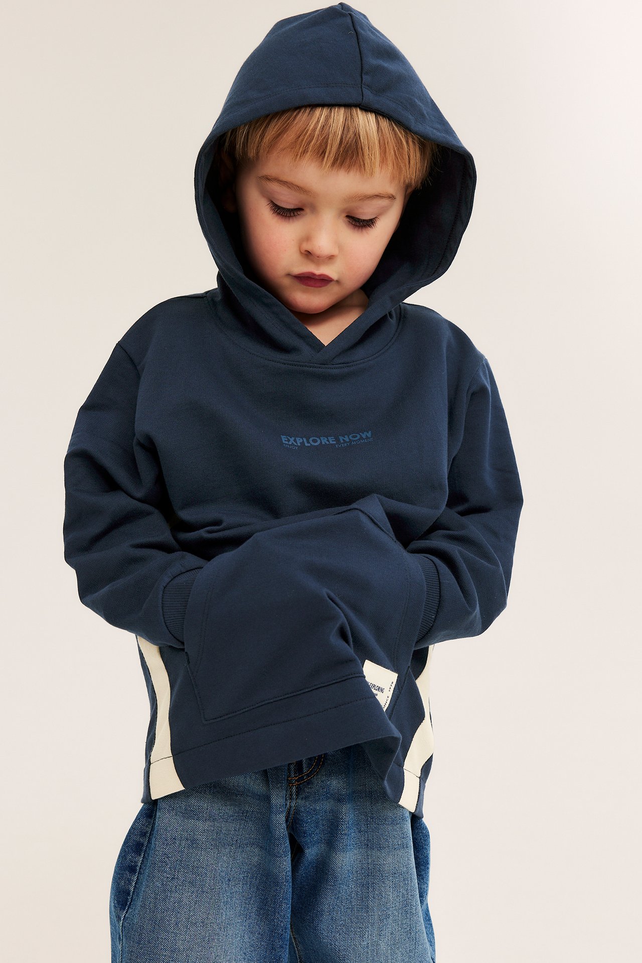 Forfra: gutt i mørk blå bomullshoodie med hvite sidepaneler og blå jeans.