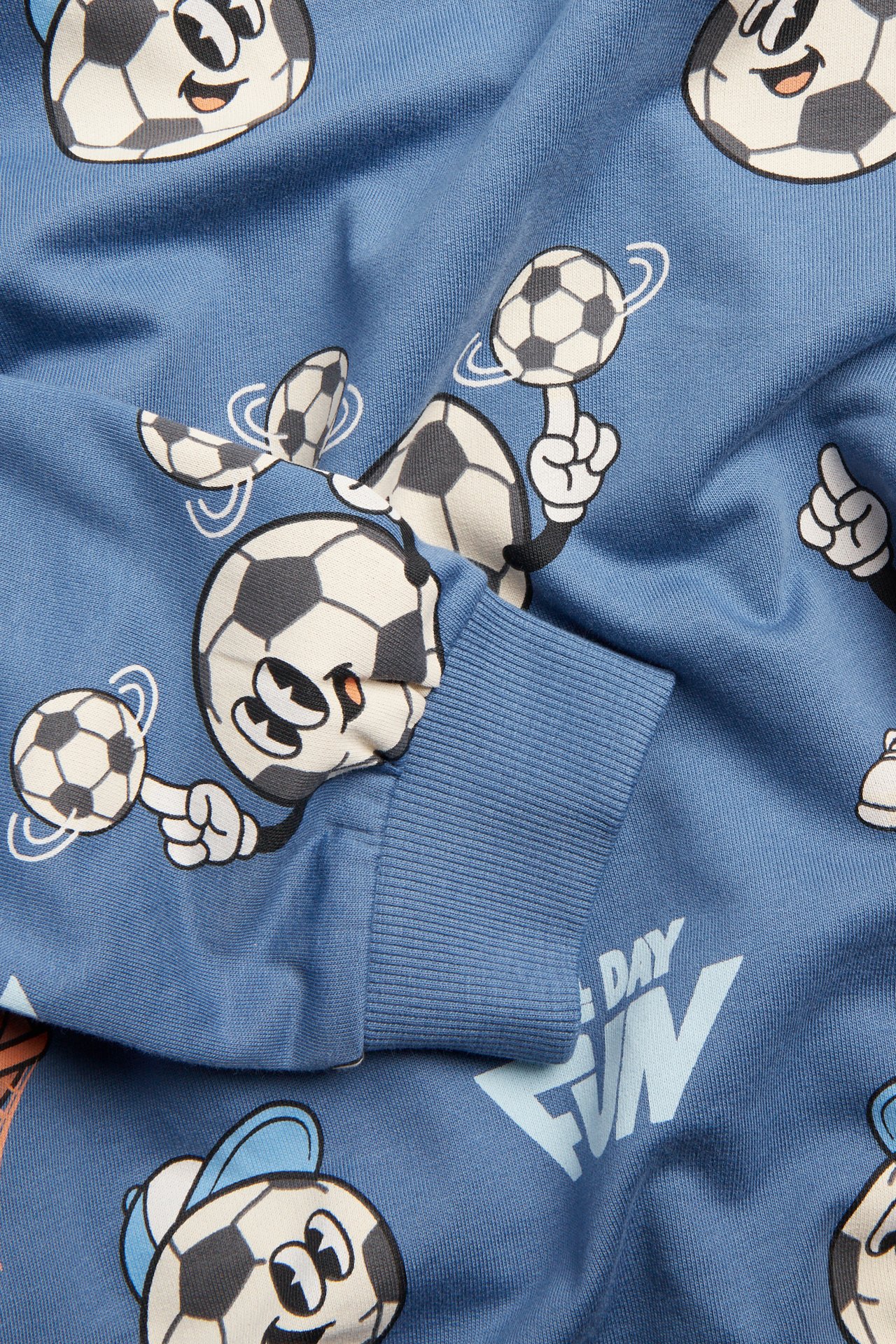 Närbild av en blå bomullssweatshirt med fotbollsmönster och ribbad mudd.