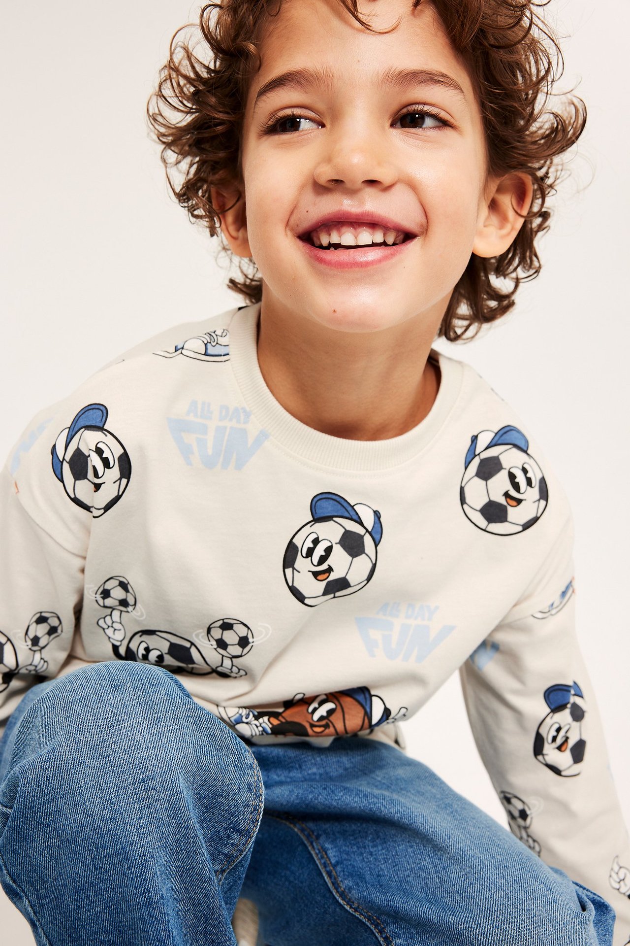 Framifrån, leende barn i ljusbeige mönstrad långärmad bomulls-t-shirt och blåa denimjeans.