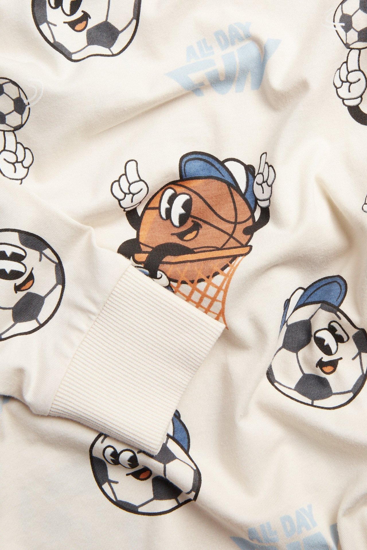 Zbliżenie beżowej bawełnianej koszulki z długim rękawem, z nadrukiem sportowych kreskówek i ściągaczami.