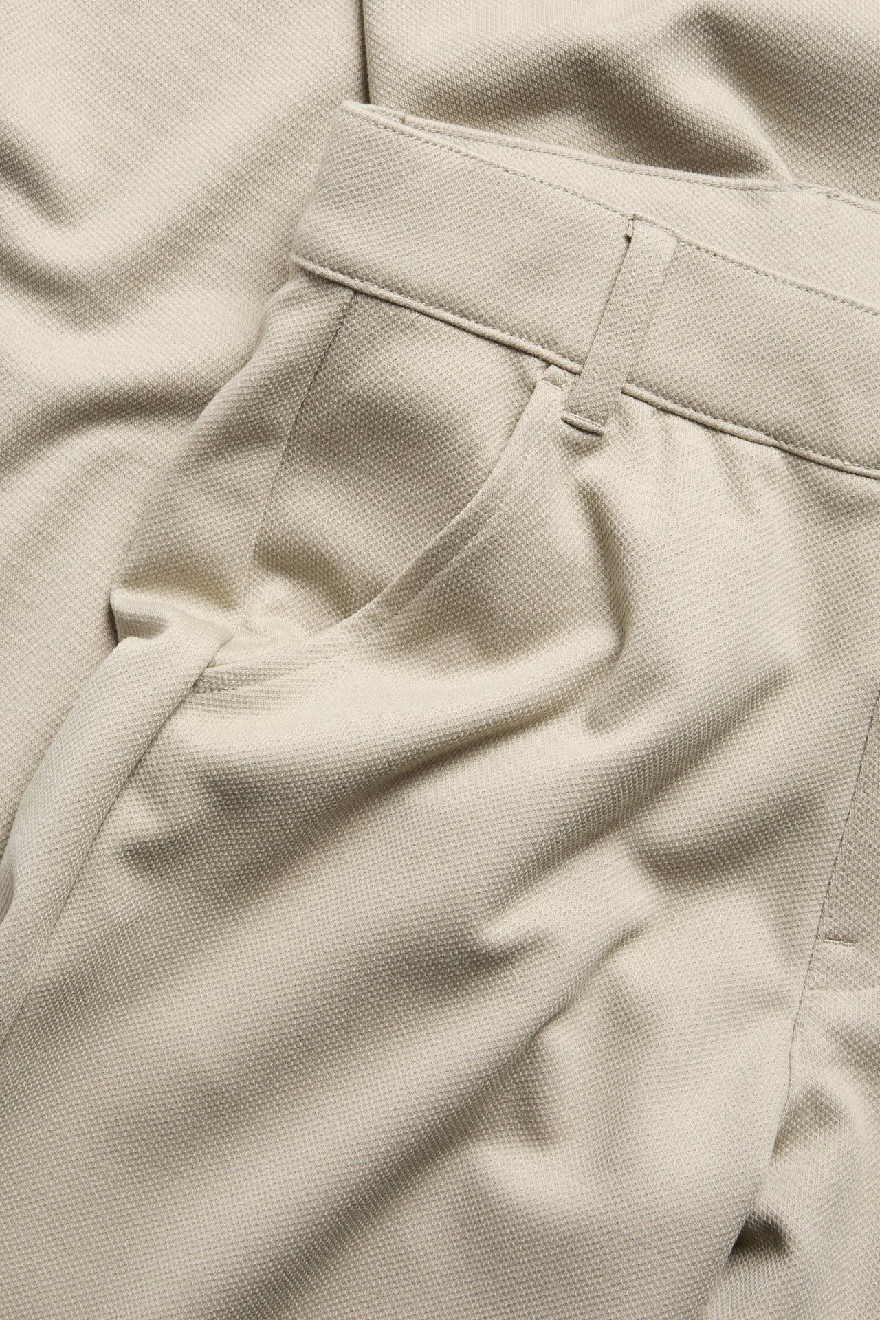 Lähikuva beigenvärisistä tekstuurisista siisteistä housuista, joissa sivutaskut ja vyölenkit.