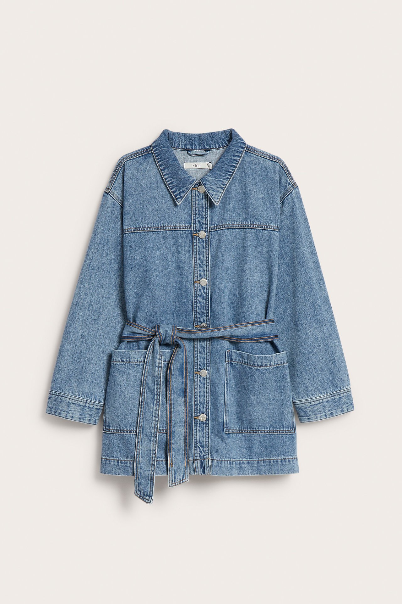Forfra: Lysblå denim shacket med knapper foran, påsydde lommer og et knyttet belte.