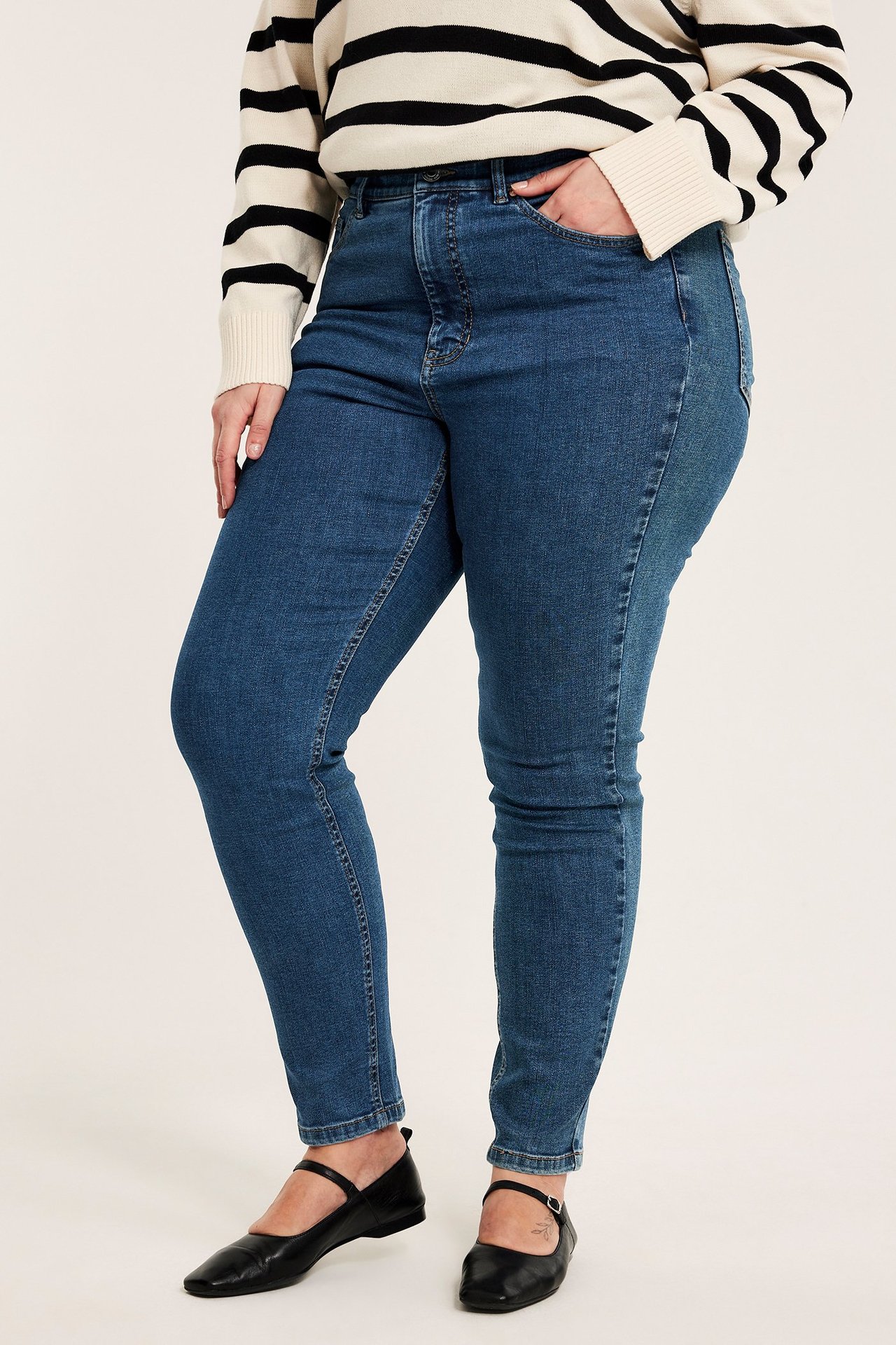 Sidovy av en kvinna i blåa slim jeans med hög midja, randig tröja och svarta ballerinaskor.