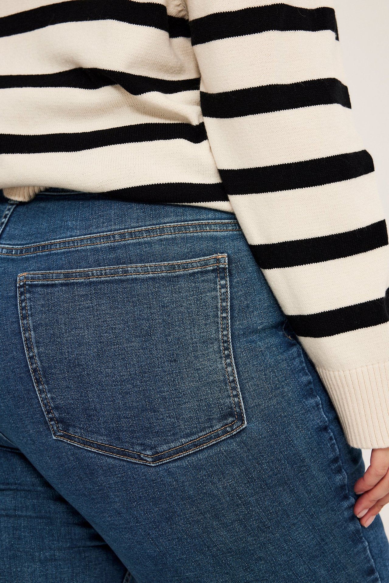 Närbild bakifrån av en kvinna i blåa slim jeans med bakficka, bärande en randig tröja.