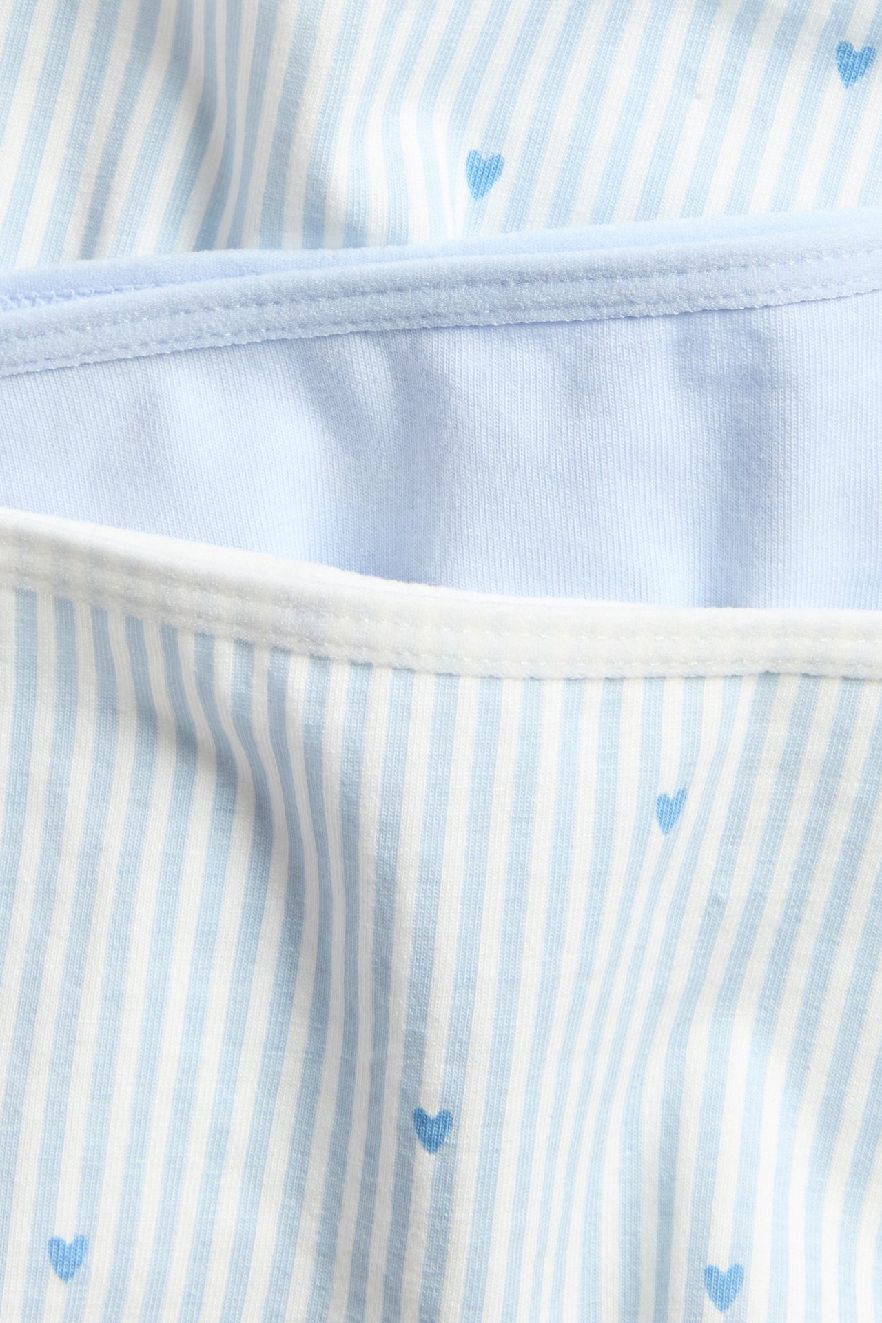 Zbliżenie na trzy bawełniane majtki typu hipster: dwa w niebieskie paski i serca, jedne gładkie jasnoniebieskie.